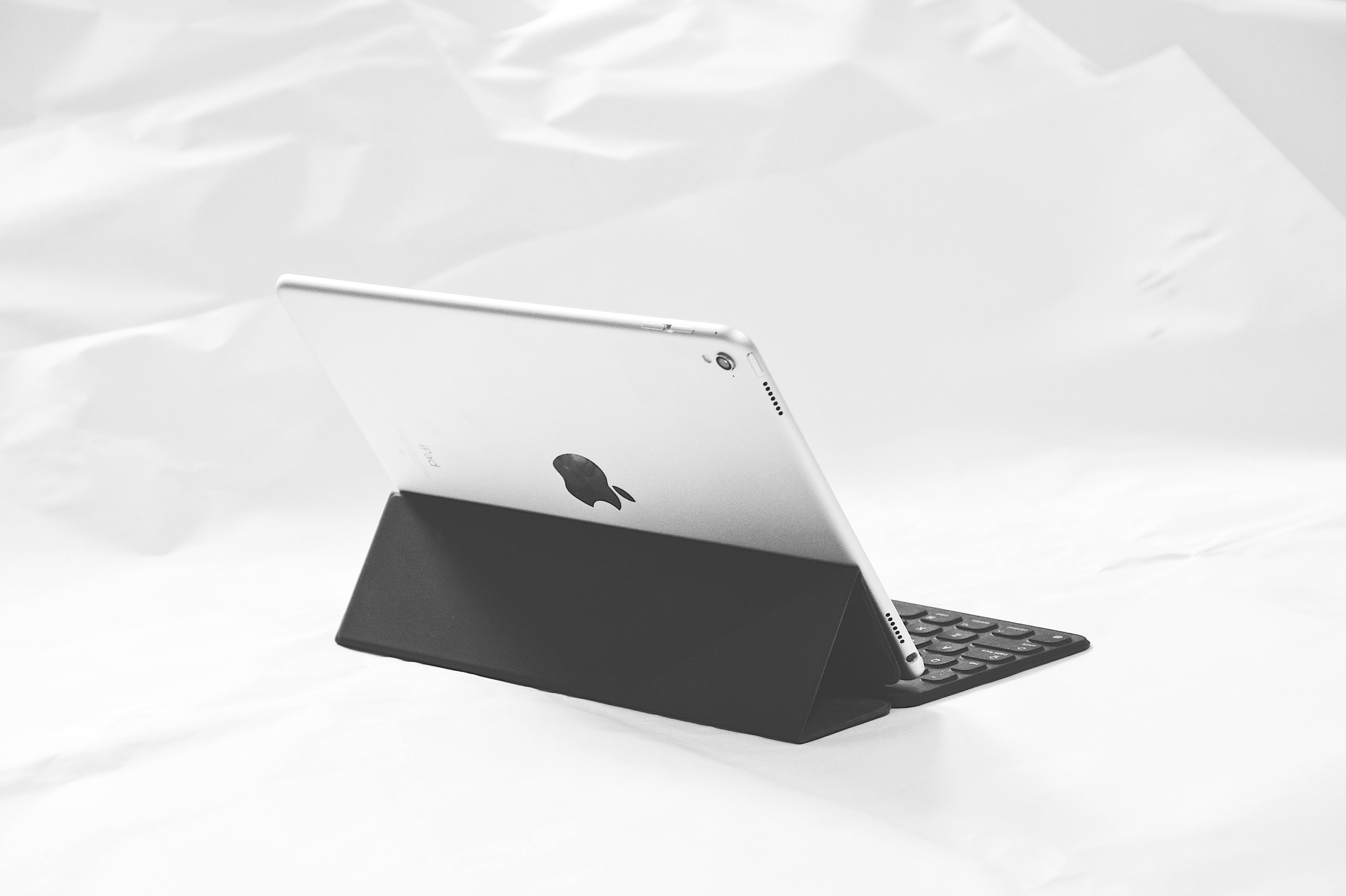 平板電腦 桌布 壁紙 — 一部時尚的銀色 iPad 帶有 Apple 標誌，放在黑色鍵盤保護殼上，置於皺褶的白色布料上，呈現極簡黑白風格。
