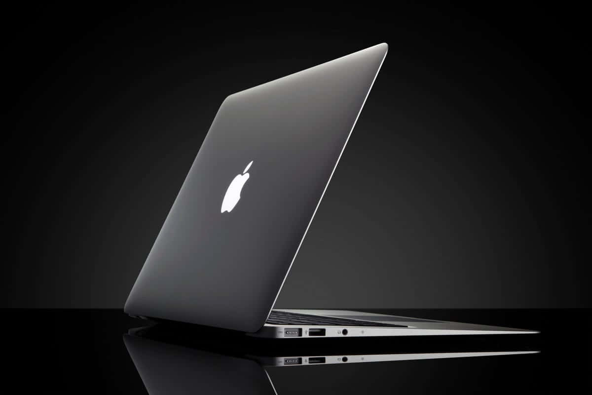 Black Macbook 桌布 壁紙 — 一部時尚的銀色 MacBook 筆記型電腦在反射黑色表面上傾斜打開，背景為深色漸變。