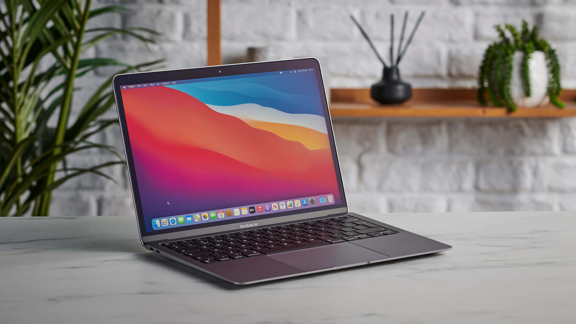 MacBook 動態圖片 桌布 壁紙 — 一部時尚的銀色 MacBook Air 打開放在大理石檯面上，螢幕上閃耀著充滿活力的抽象桌布。
