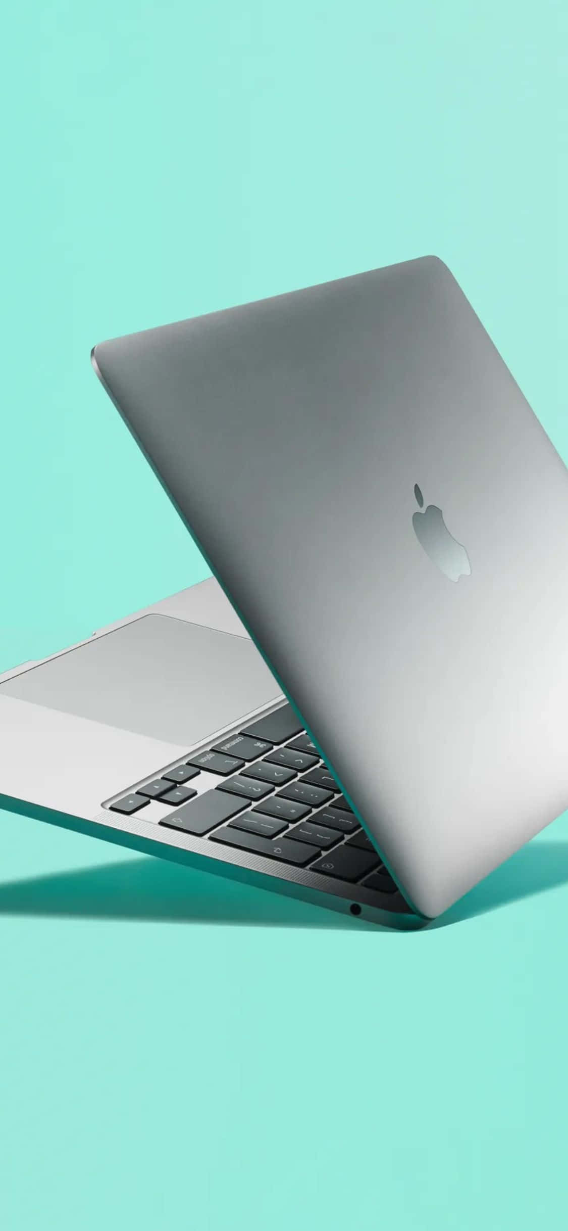 iPhone Xs Computer 桌布 壁紙 — 一部時尚的銀色 MacBook 筆記型電腦斜開在純薄荷綠色背景上。