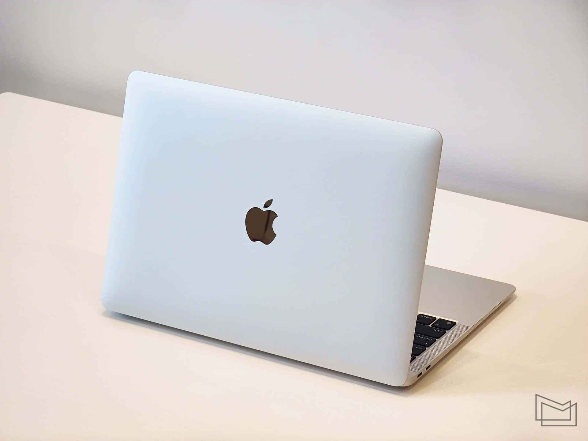 MacBook 動態圖片 桌布 壁紙 — 一部時尚的銀色 MacBook 筆記型電腦在柔和日光下打開，放在簡約的白色桌子上。