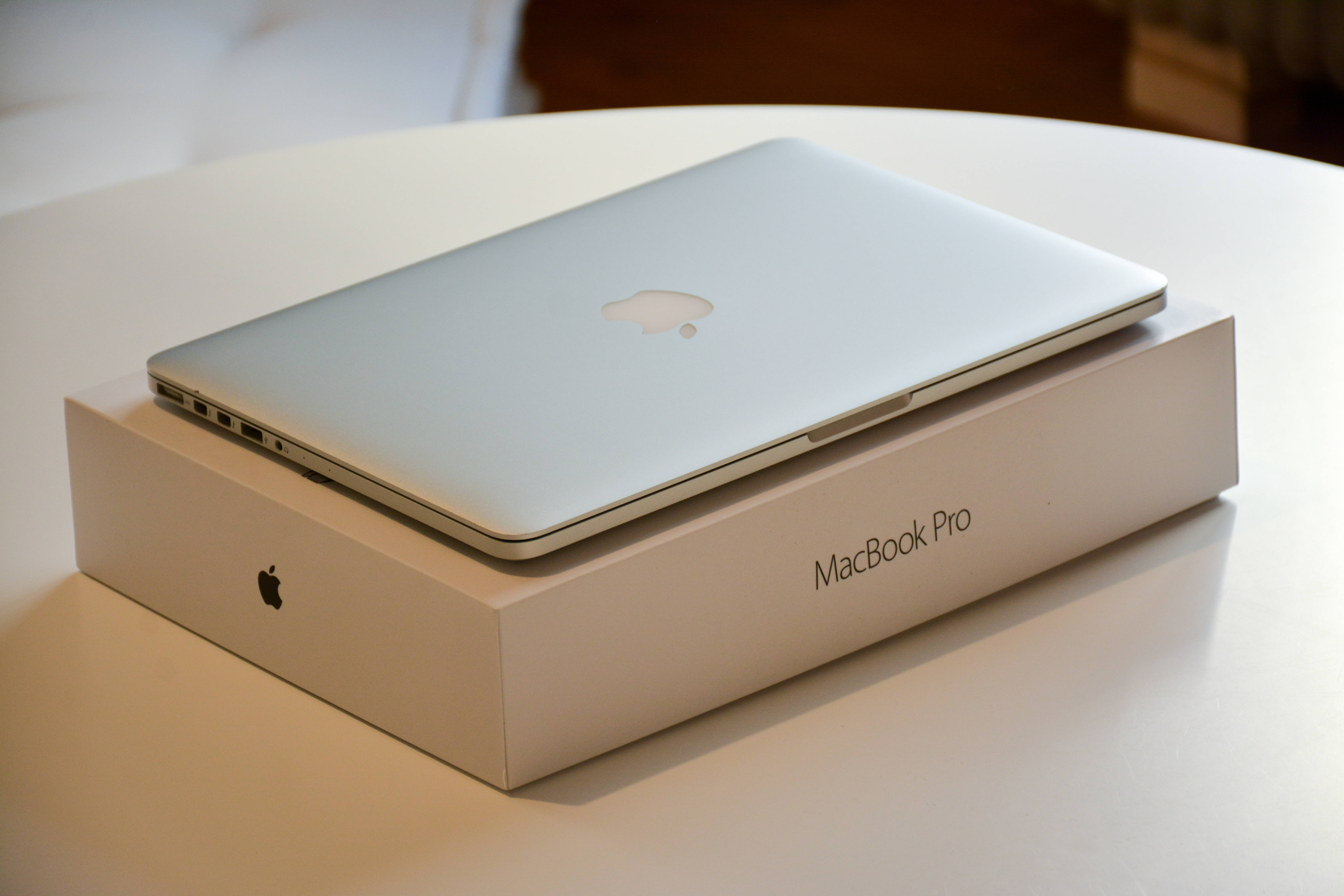 MacBook 動態圖片 桌布 壁紙 — 一部時尚的銀色 MacBook Pro 放在其白色包裝盒上，置於簡約的白色桌子上，柔和日光下。
