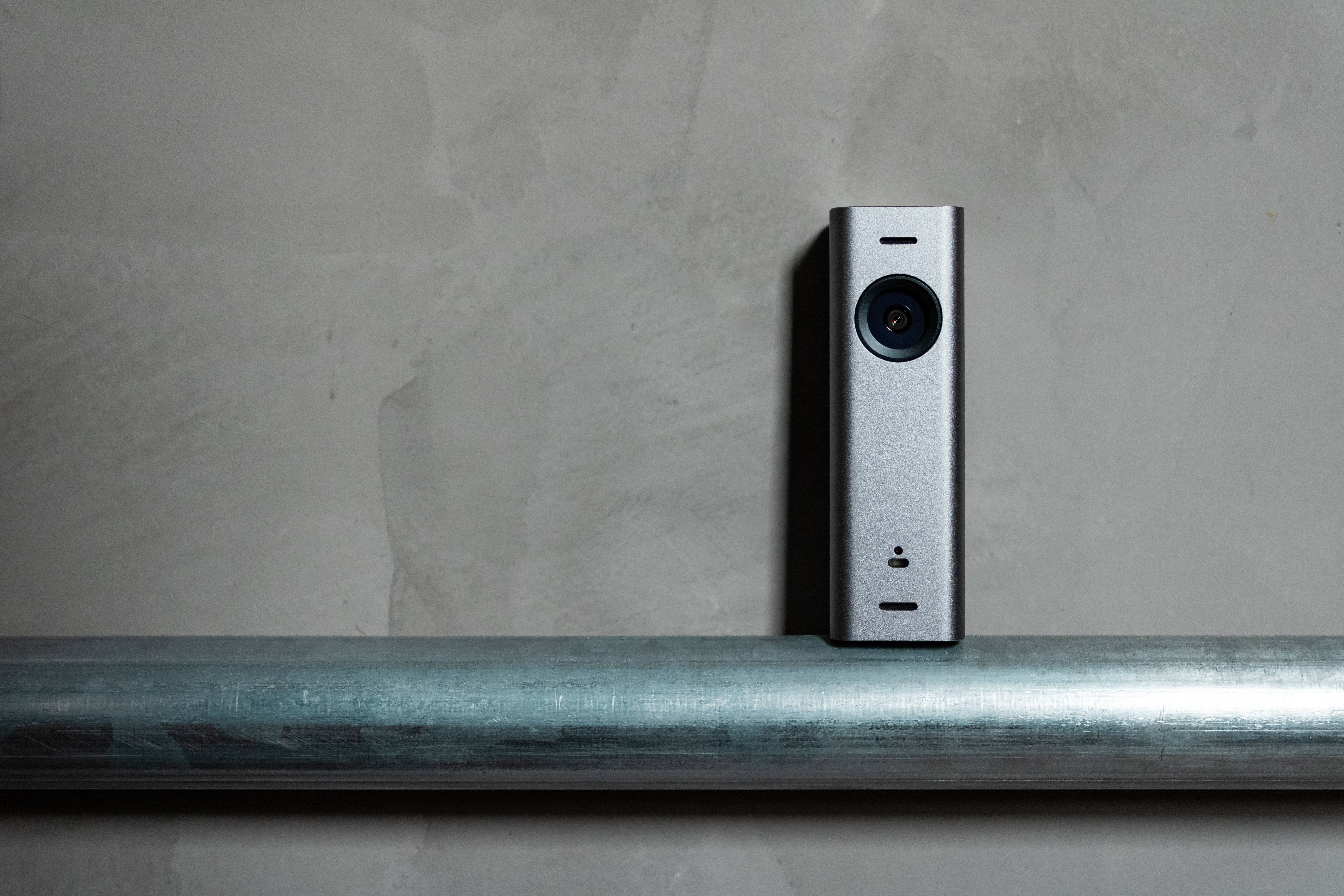 Webcam 桌布 壁紙 — 一部時尚的銀色360度相機放置在拉絲金屬管上，背景是紋理混凝土牆。