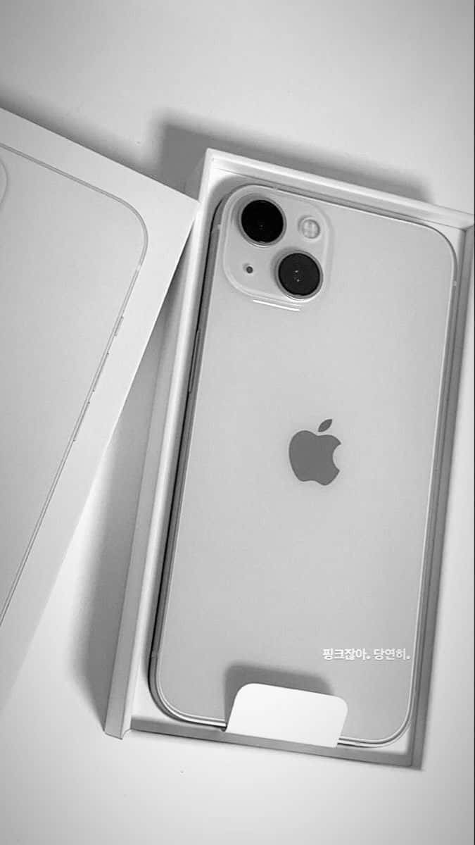iPhone 12 桌布 壁紙 — 一部時尚的銀色iPhone安放在打開的盒子中，極簡的單色燈光突出其相機和標誌。