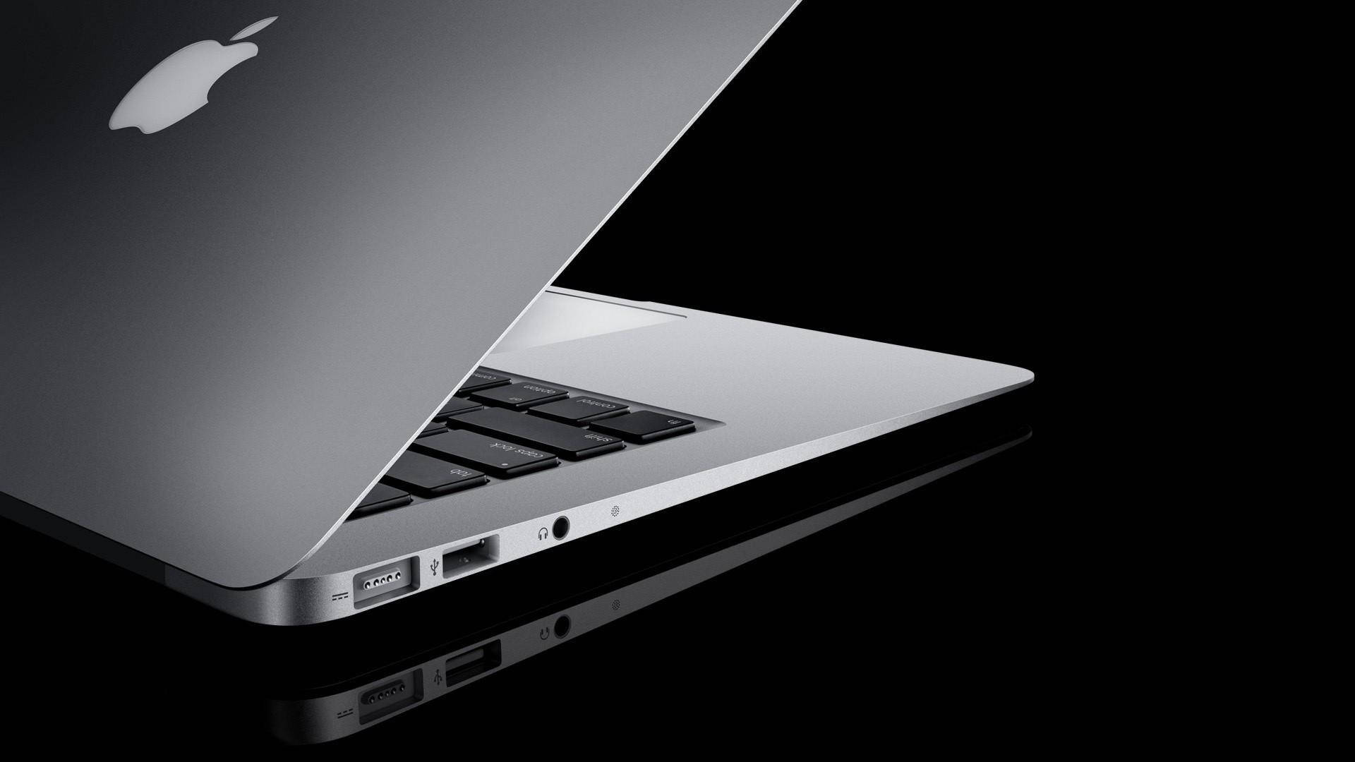 MacBook 動態圖片 桌布 壁紙 — 一部時尚的銀色MacBook筆記型電腦傾斜打開，放在黑色反光表面上，展示其連接埠和鍵盤。