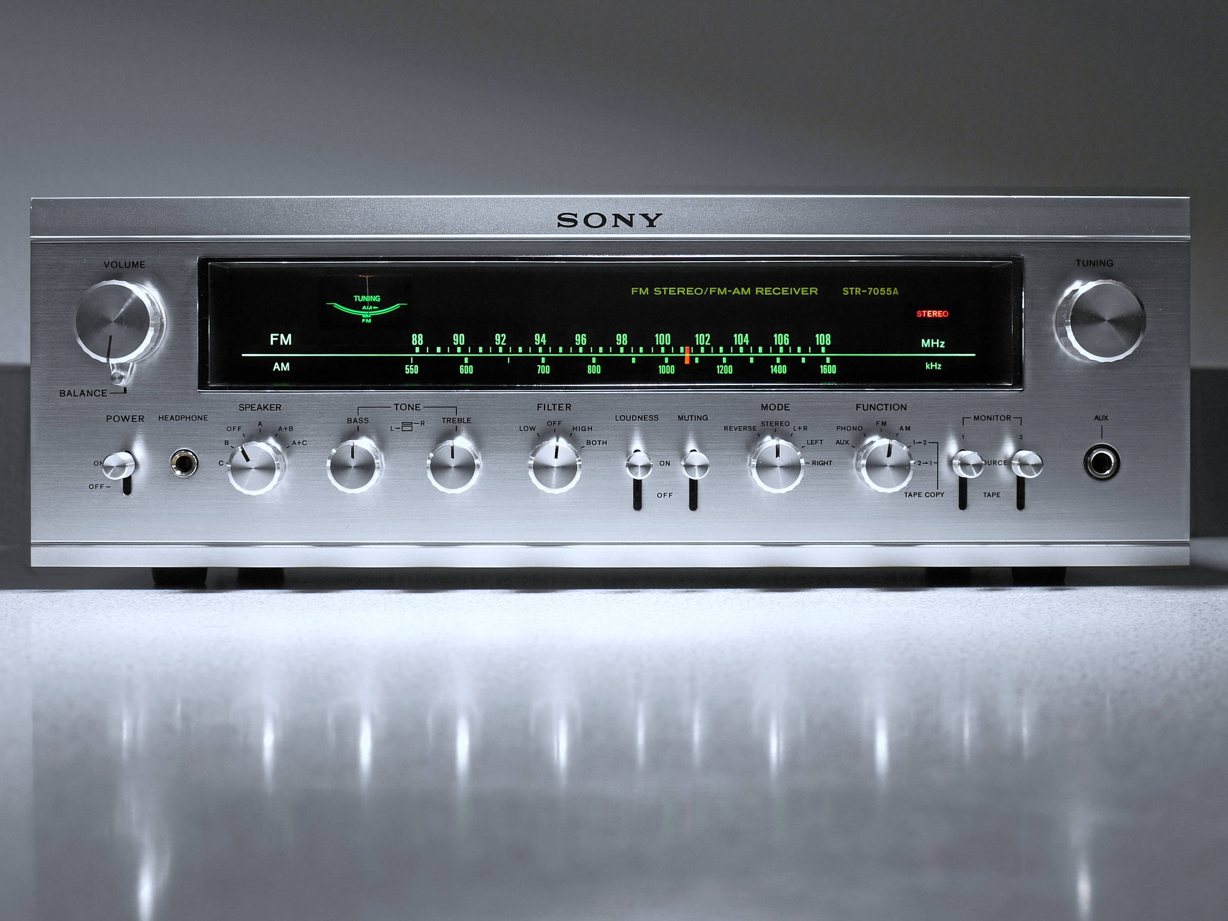 Sony 桌布 壁紙 — 一部時尚的銀色Sony立體聲接收器，在攝影棚燈光下置於反光表面，帶有發光的綠色刻度盤和旋鈕。