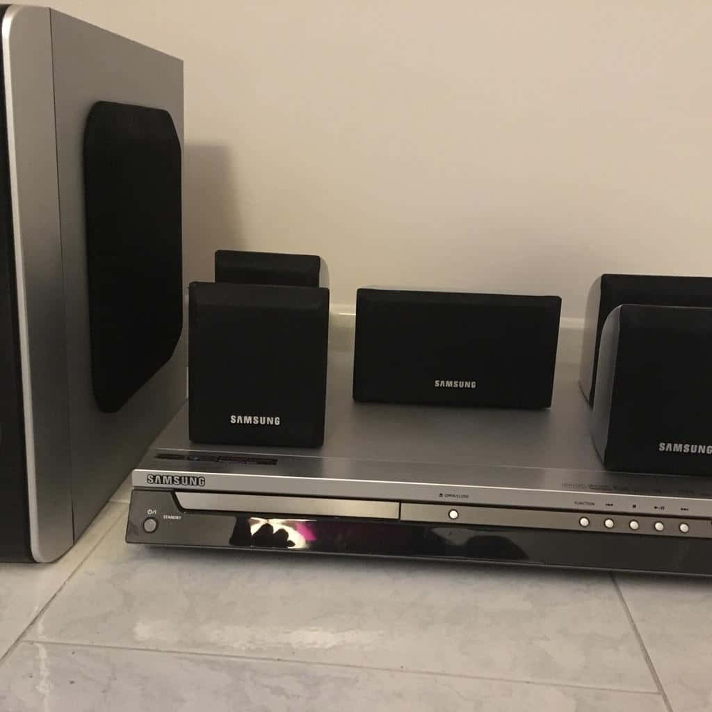 三星 桌布 壁紙 — 一部時尚的銀色三星DVD播放器搭配黑色揚聲器，放在白色瓷磚地板上，靠著素牆。