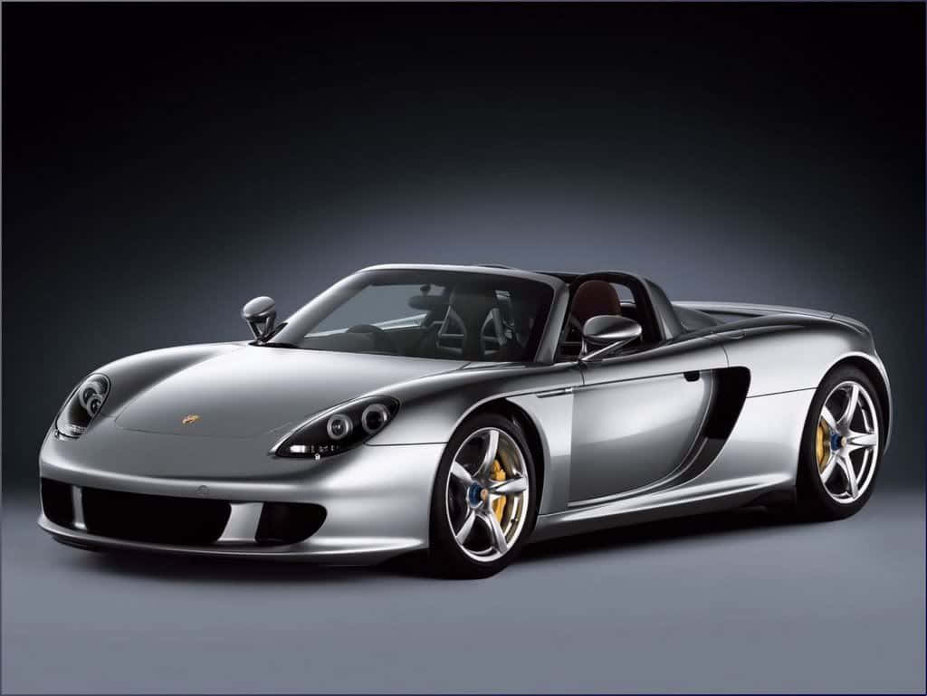 保時捷 桌布 壁紙 — 一部時尚的銀色保時捷 Carrera GT 敞篷跑車，配備金色制動卡鉗，在深色漸變工作室背景前展示。
