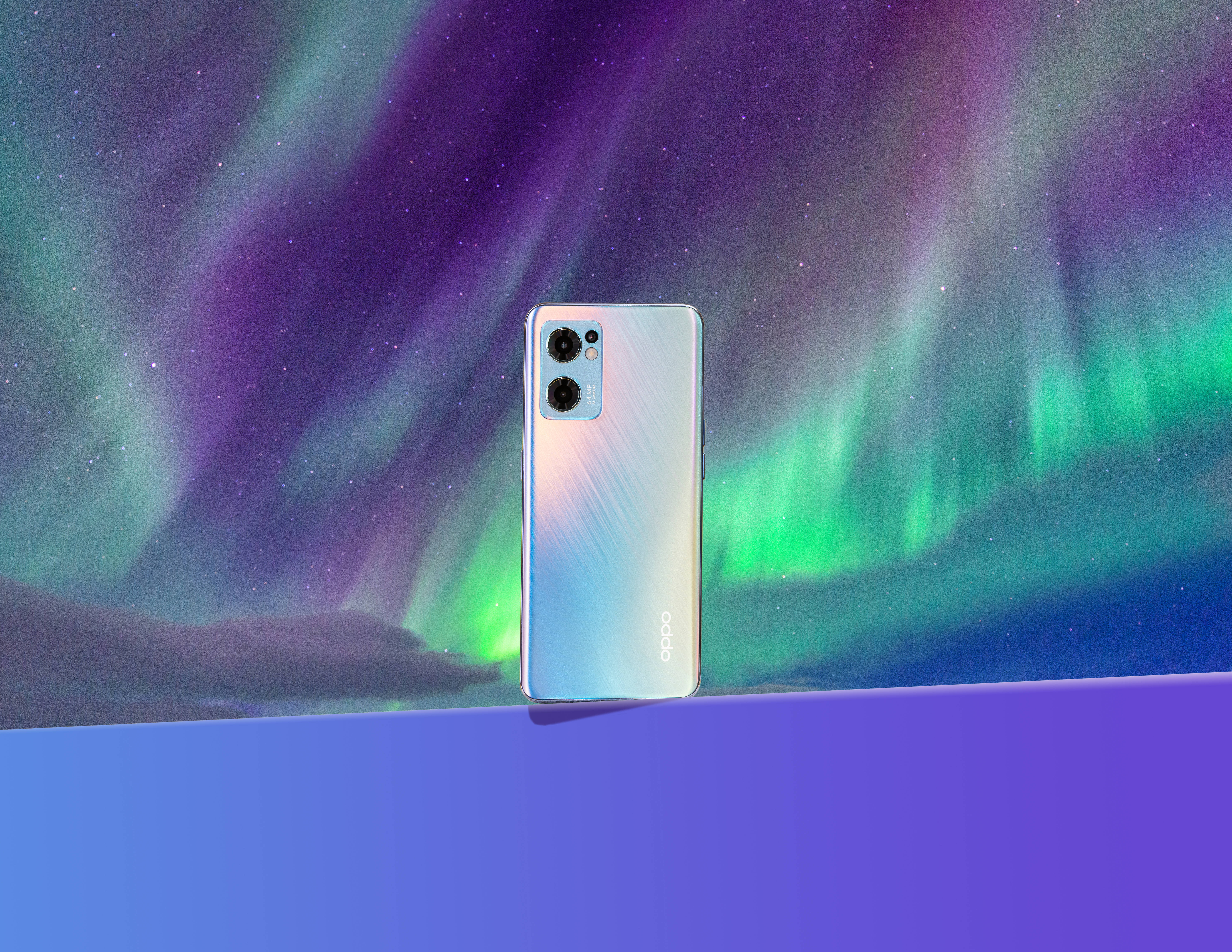 oppo 桌布 壁紙 — 一部時尚的銀色智慧型手機直立於充滿活力的北極光背景前，帶有紫色、綠色和藍色色調。