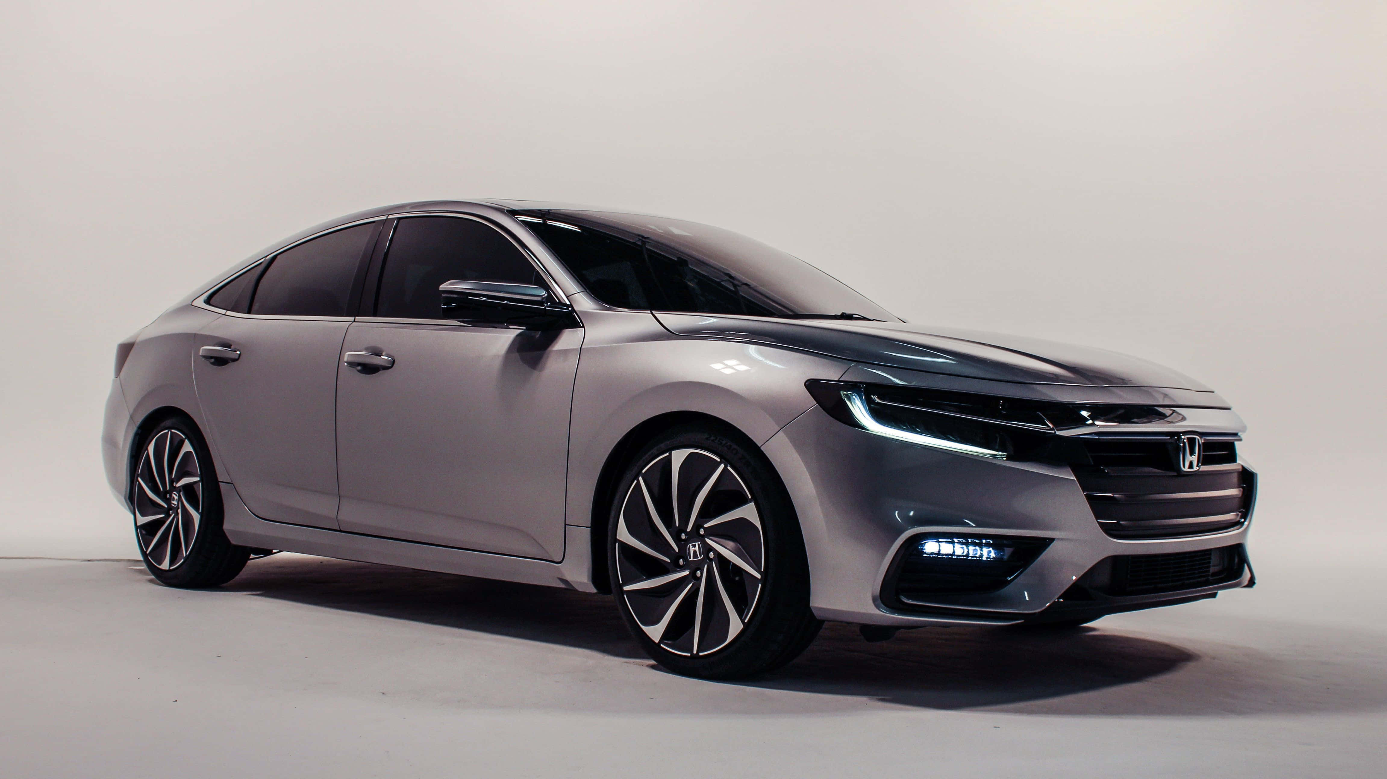 Honda Insight 桌布 壁紙 — 一部時尚的銀色本田轎車，配備未來感車頭燈和時尚合金輪圈，在簡約的白色工作室背景前展示。