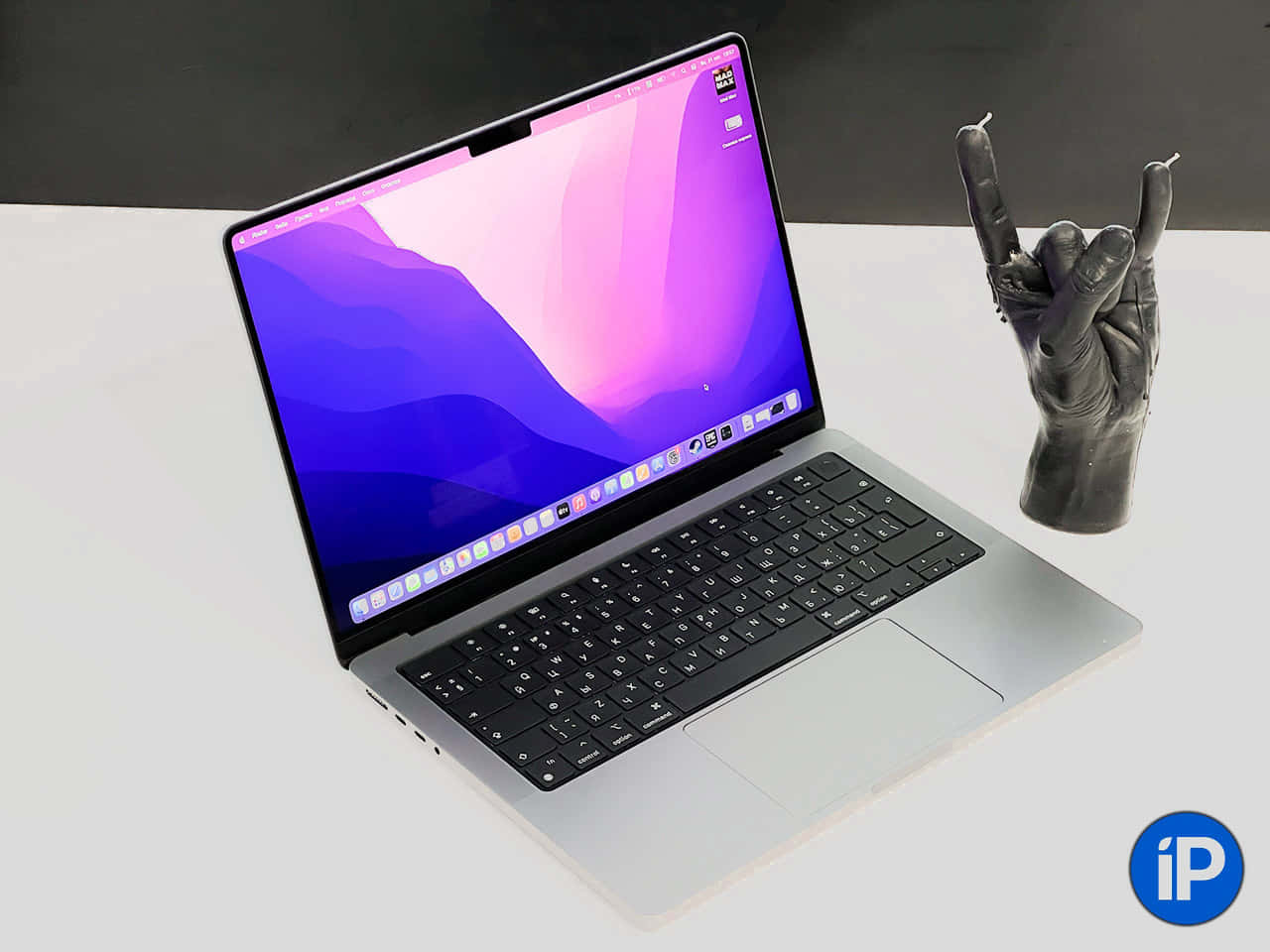 Mac 桌布 壁紙 — 一部時尚的銀色筆記型電腦，帶有充滿活力的紫色和藍色抽象桌布，旁邊是一個黑色皮革搖滾手勢雕像，放在白色表面上。