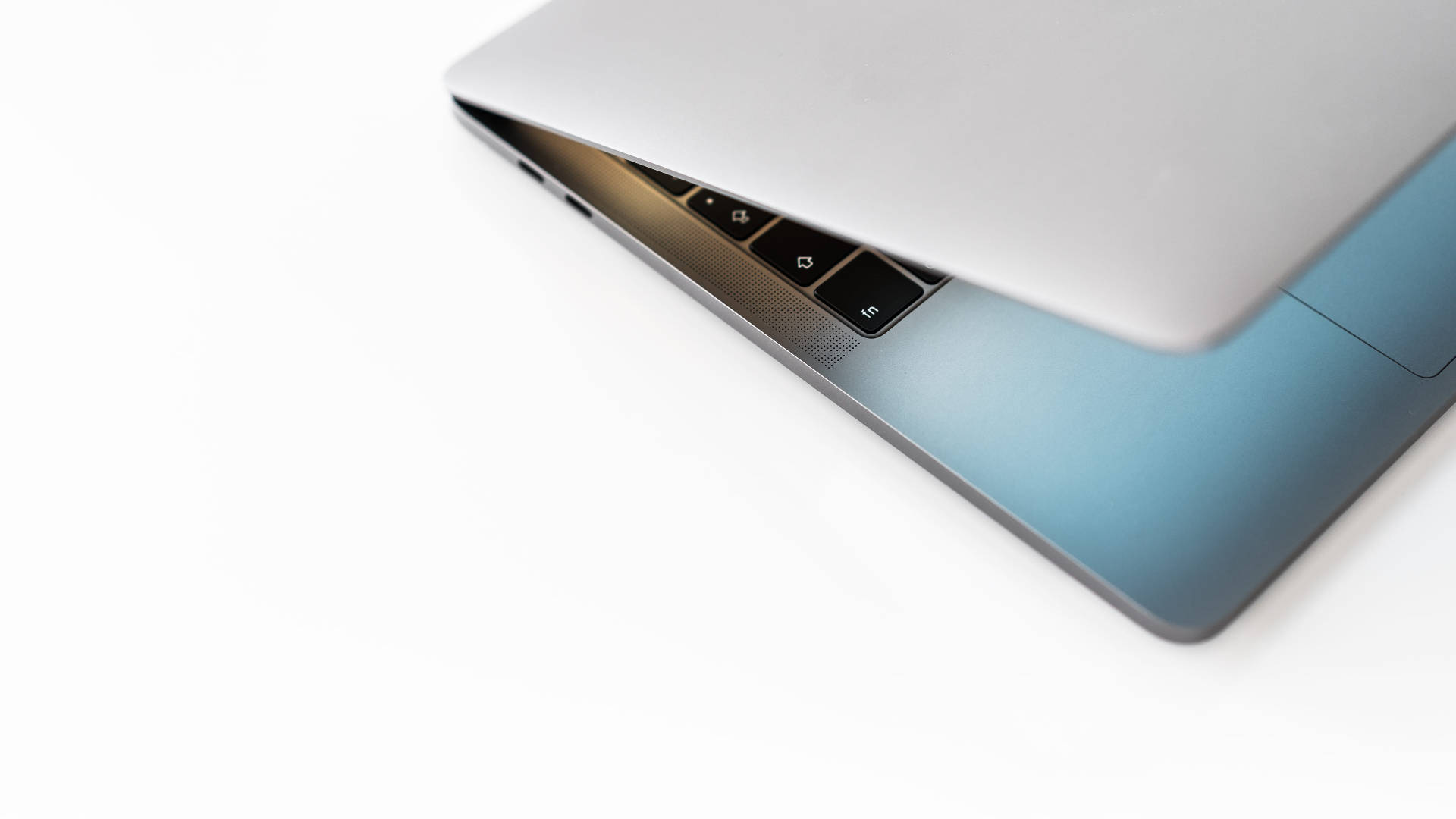 MacBook 動態圖片 桌布 壁紙 — 一部時尚的銀色筆記型電腦，帶有藍色漸層底座，打開放在純白表面上。