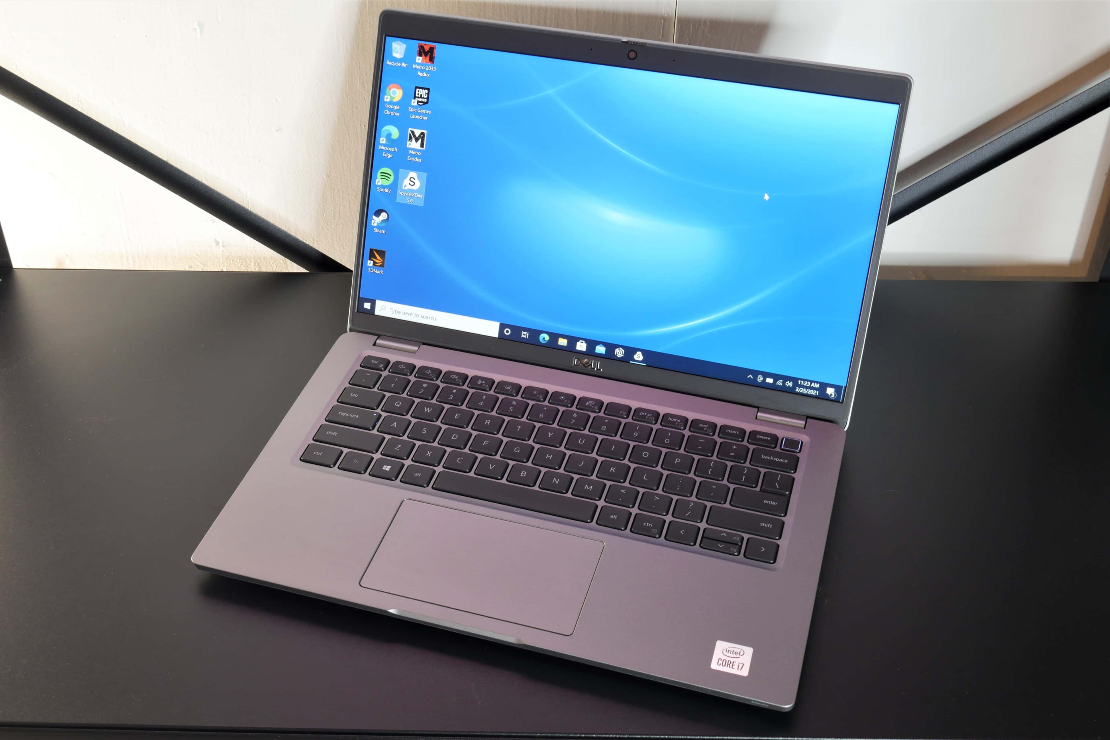 Dell 桌布 壁紙 — 一部時尚的銀色筆記型電腦，顯示藍色Windows桌面，打開放在黑色桌子上，背景是簡約的白色牆壁。