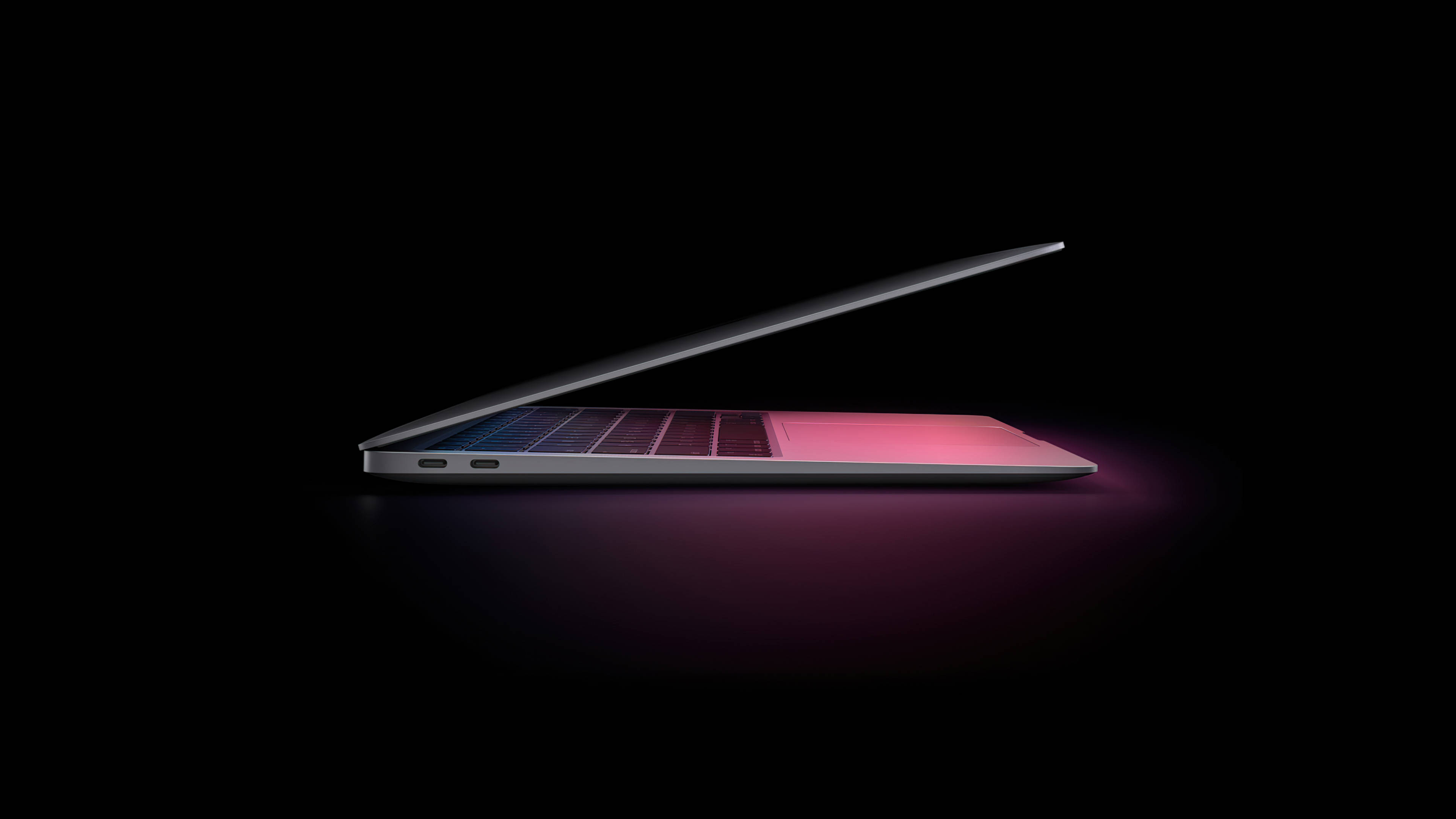 MacBook 動態圖片 桌布 壁紙 — 一部時尚的銀色筆記型電腦以傾斜角度打開，置於黑色背景上，帶有發光的粉紅色和藍色背光。