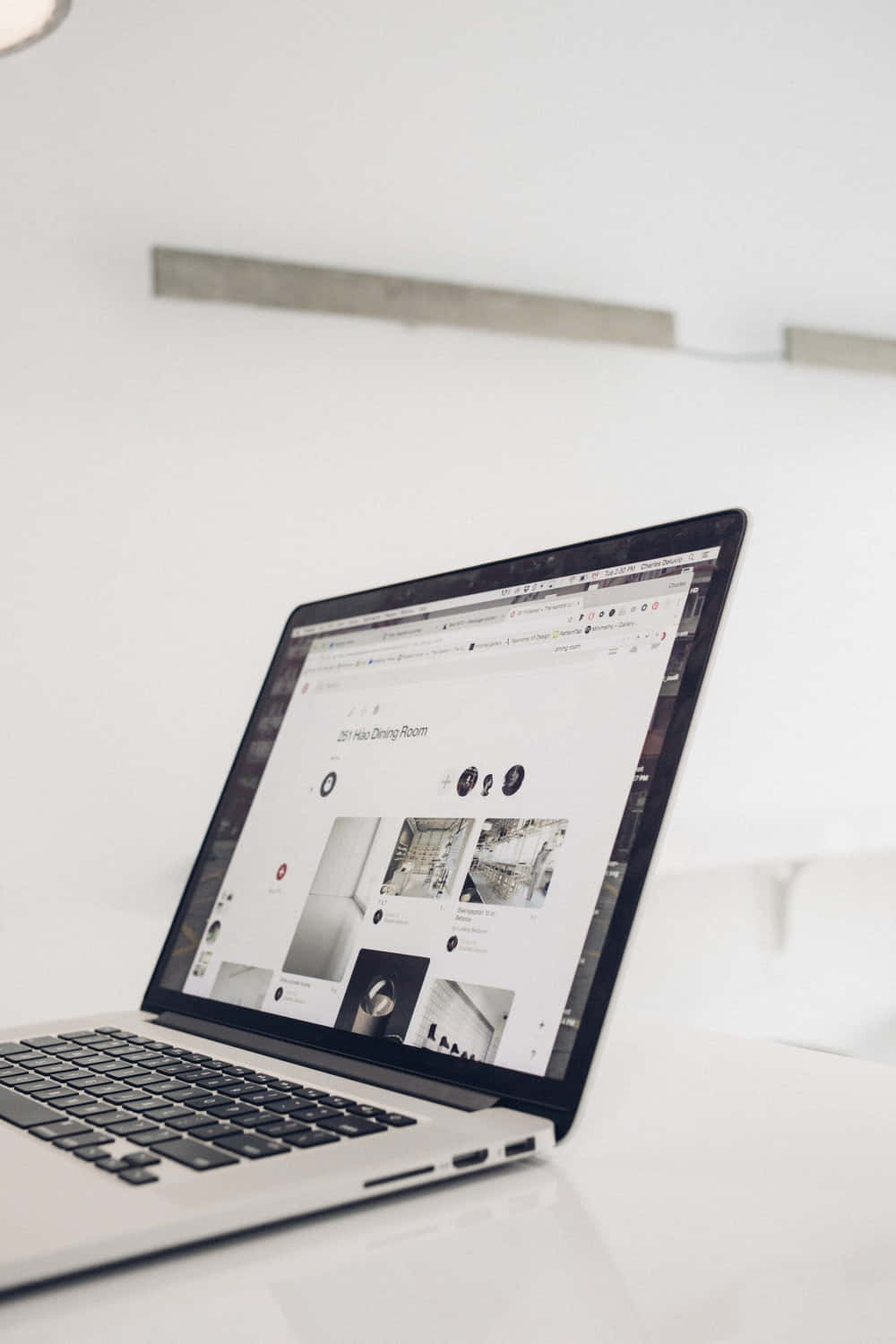 Website 桌布 壁紙 — 一部時尚的銀色筆記型電腦在柔和的自然光下，於明亮的白色桌子上顯示一個極簡主義的室內設計網站。