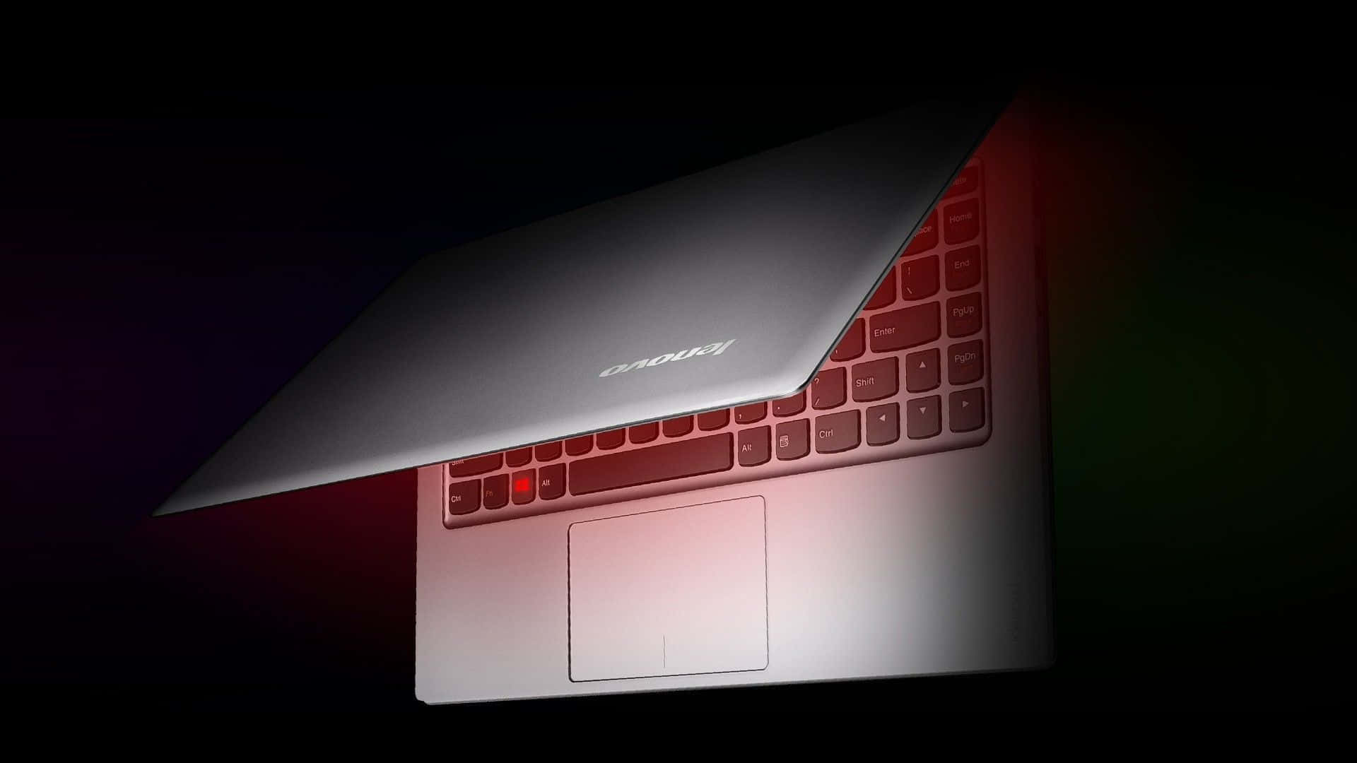 Lenovo 桌布 壁紙 — 一部時尚的銀色筆記型電腦在黑暗背景下傾斜打開，紅色環境照明突顯其鍵盤和觸控板。
