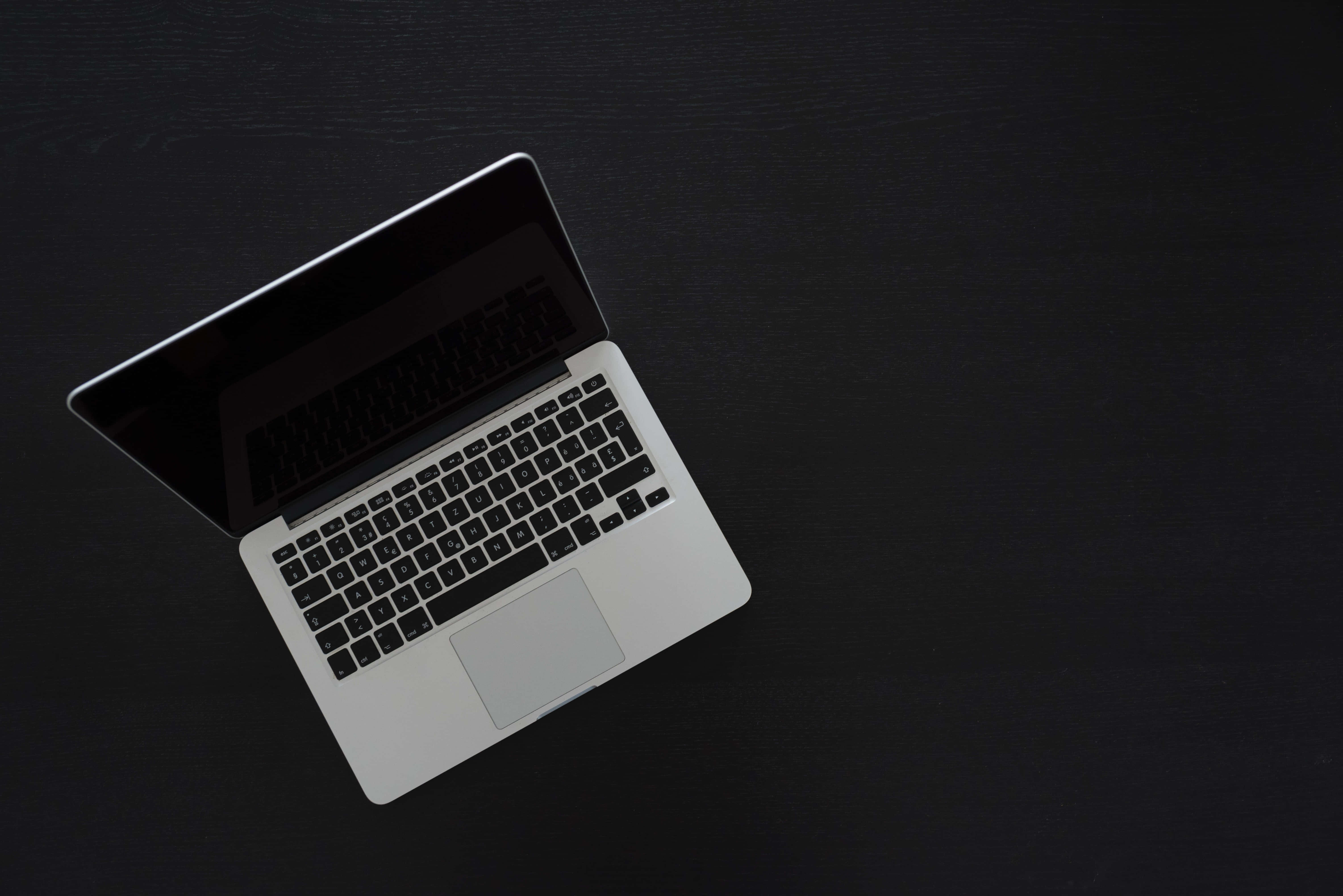 美學 MacBook 壁紙 桌布 壁紙 — 一部時尚的銀色筆記型電腦對角放置在霧面黑色表面上，簡約而現代。