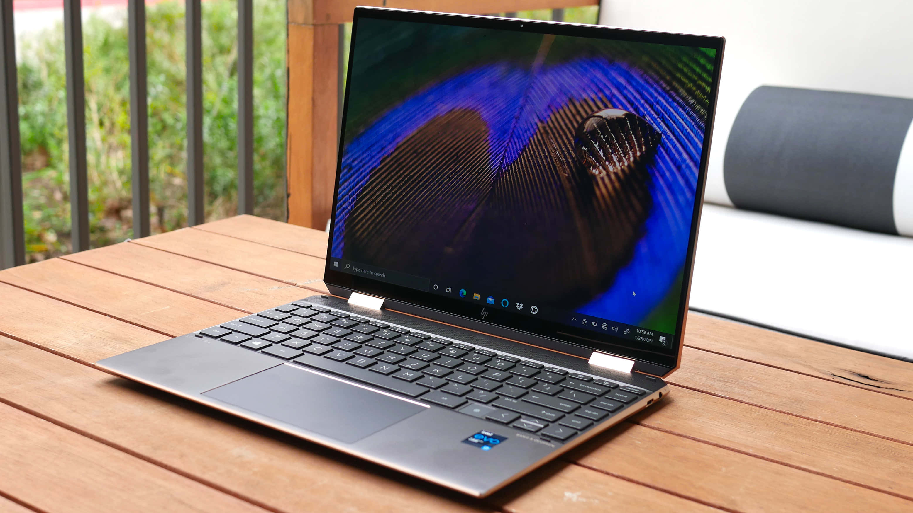 HP 桌布 壁紙 — 一部時尚的銀色筆記型電腦打開放在木桌上，顯示鮮豔的藍色和棕色孔雀羽毛桌布。