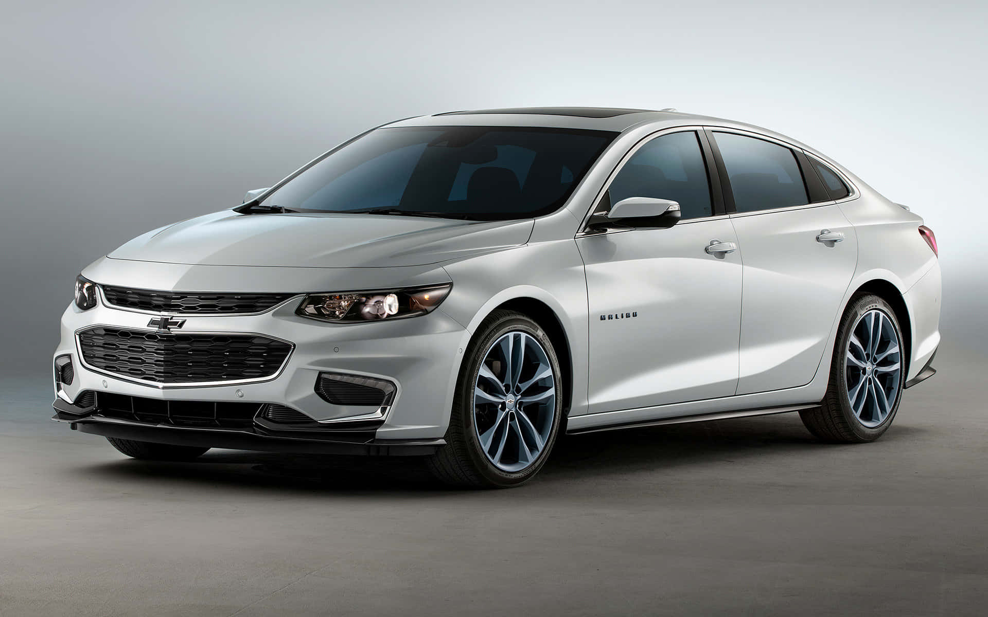 chevy 桌布 壁紙 — 一部時尚的銀色雪佛蘭 Malibu 轎車配備藍色合金輪圈，在簡約的工作室環境中展示。