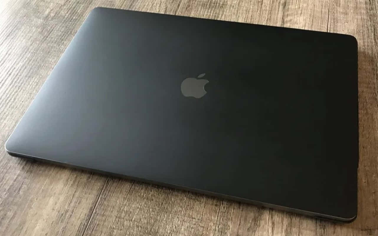 Black Macbook 桌布 壁紙 — 一部時尚的黑色 Apple 筆記型電腦闔上，放置在具有自然木紋的紋理木質表面上。