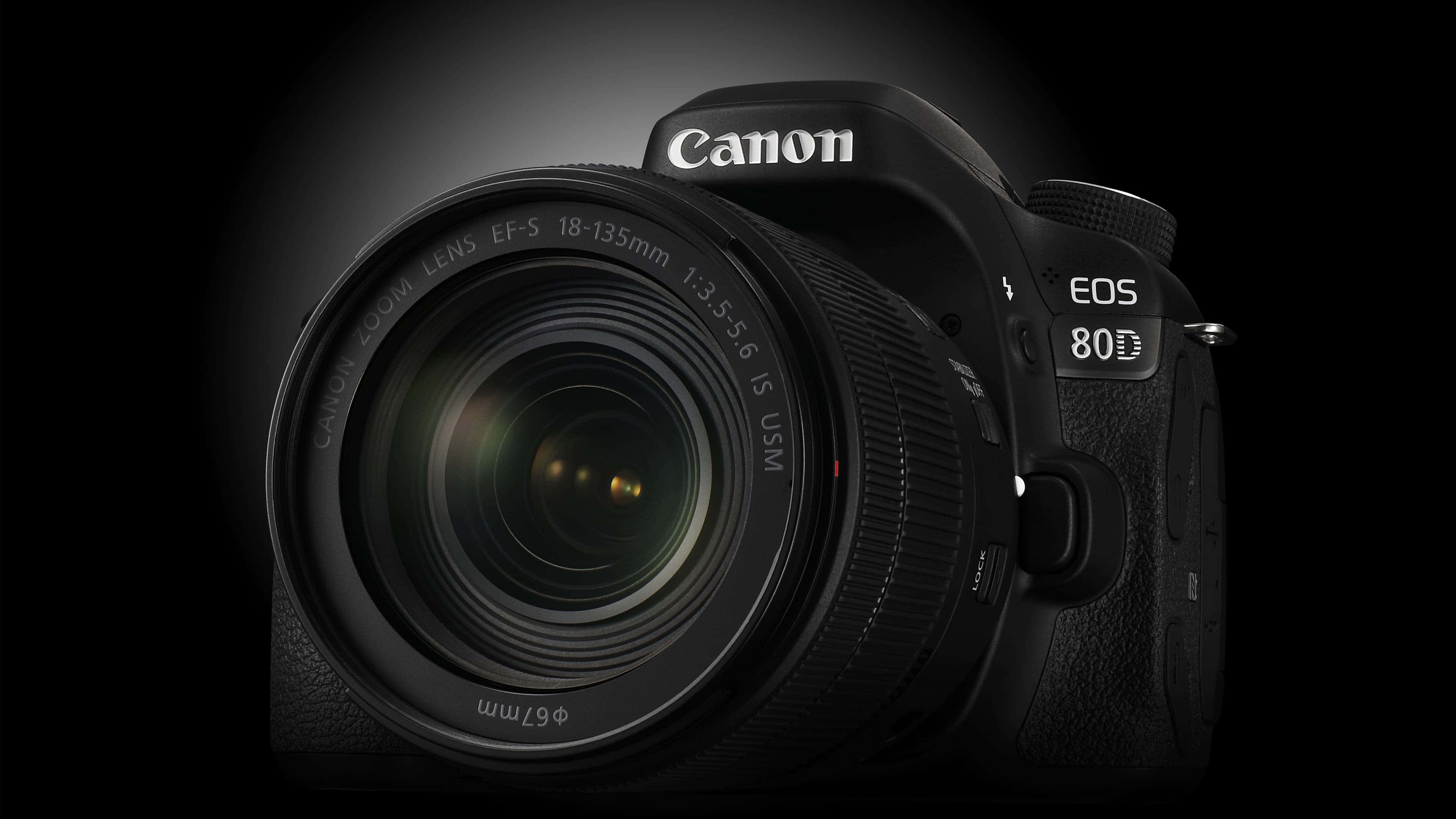 Dslr 桌布 壁紙 — 一部時尚的黑色 Canon EOS 80D DSLR 相機，配備 18-135mm 鏡頭，在深色漸變背景上照亮。