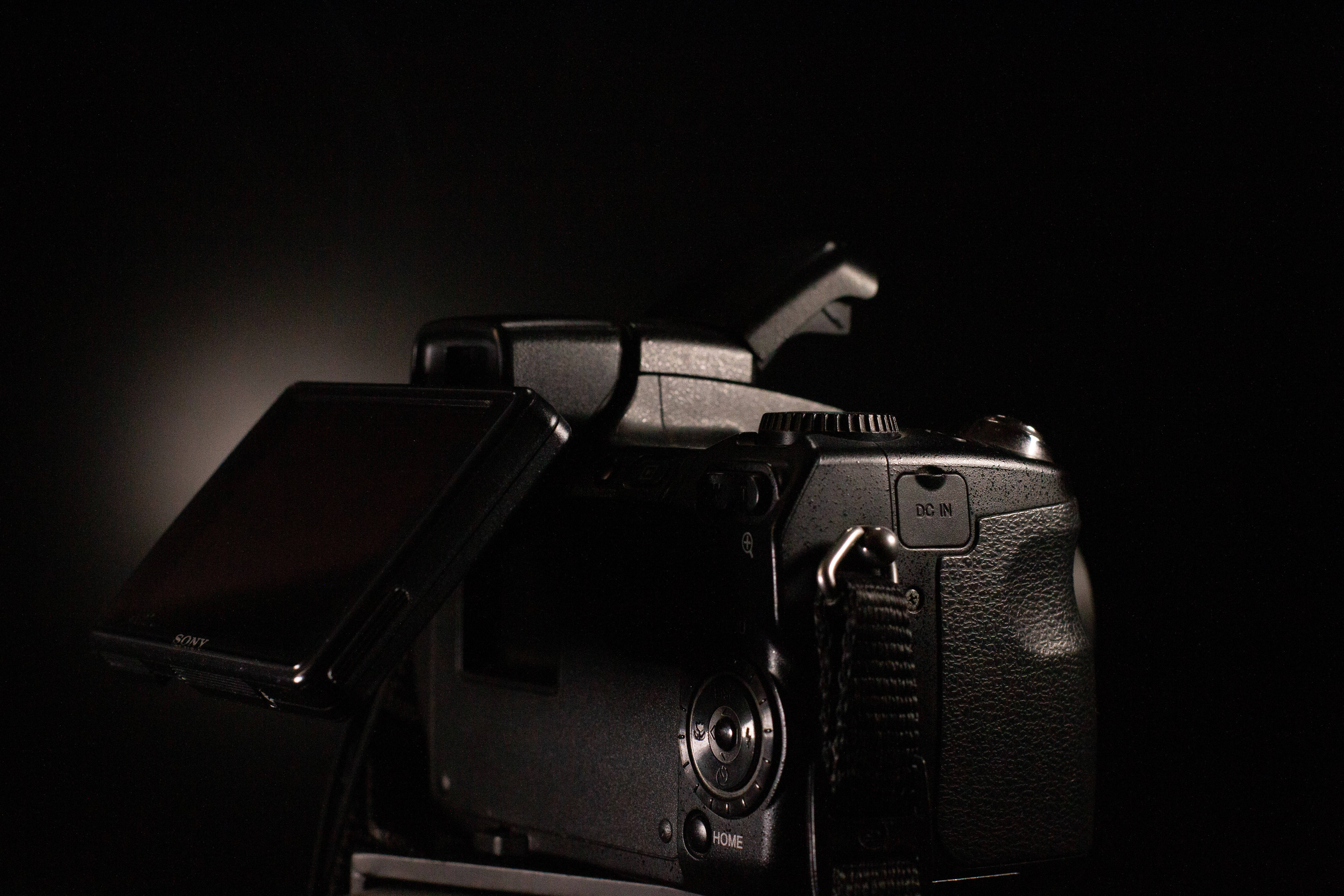 相機 桌布 壁紙 — 一部時尚的黑色 DSLR 相機，在黑暗背景下背光，其紋理手柄和翻出螢幕上帶有發光高光。