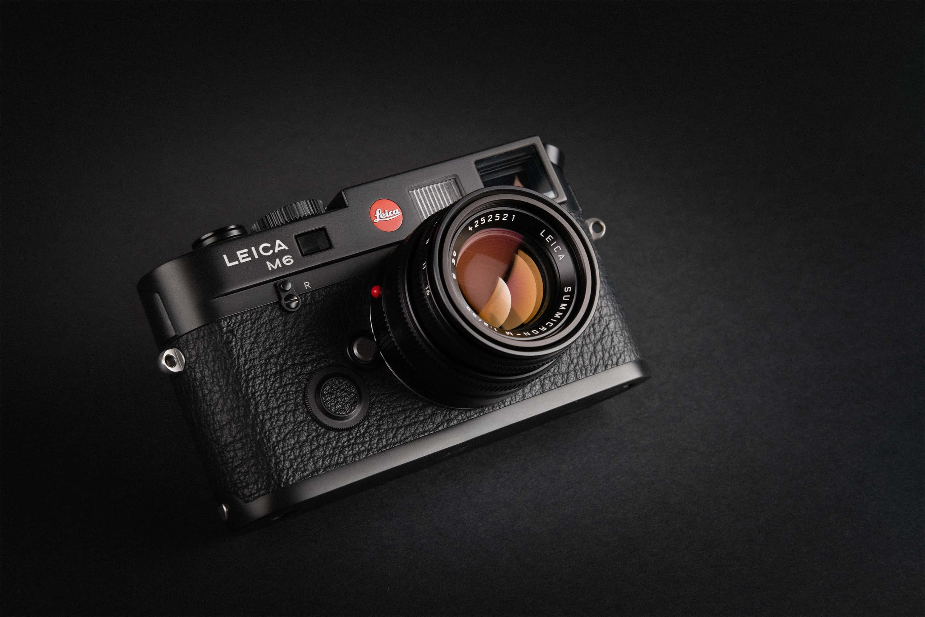 相機 桌布 壁紙 — 一部時尚的黑色 Leica M6 底片相機放置在深色表面上，鏡頭反射出溫暖的光線。