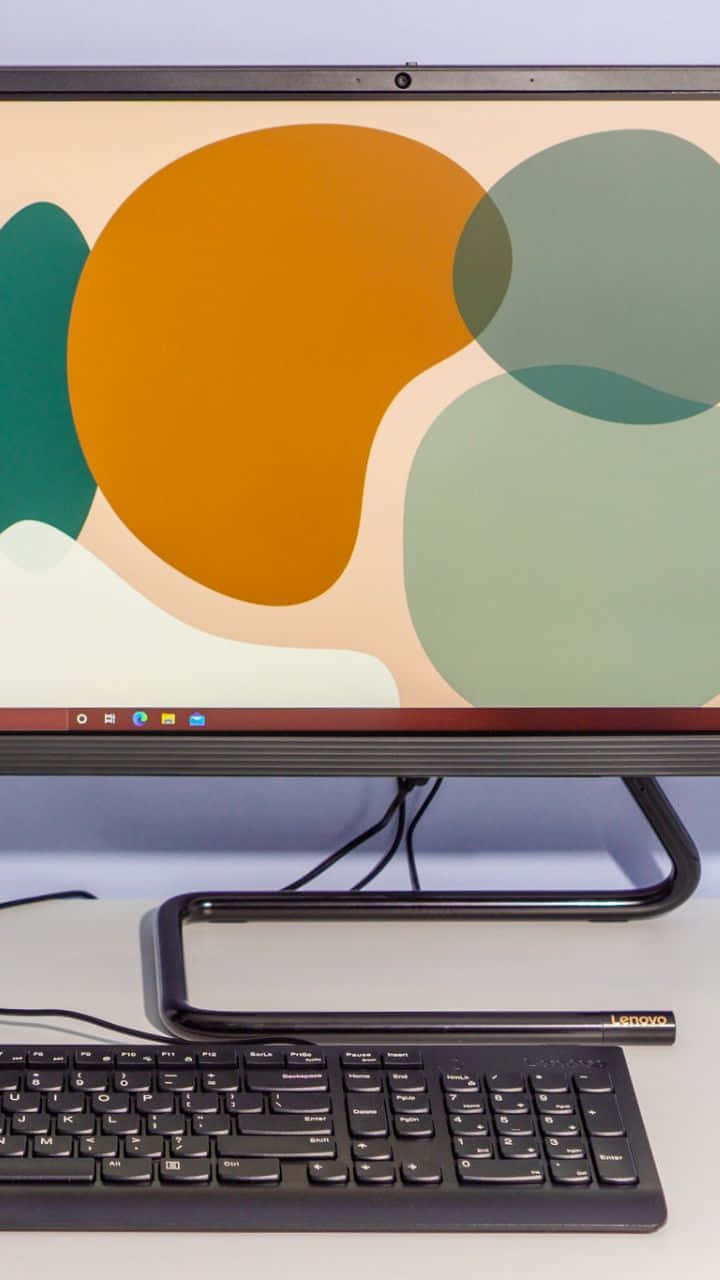 Android Computer 桌布 壁紙 — 一部時尚的黑色 Lenovo 一體式桌面電腦，螢幕上顯示著充滿活力的抽象桌布，包含橙色、綠色和奶油色形狀。