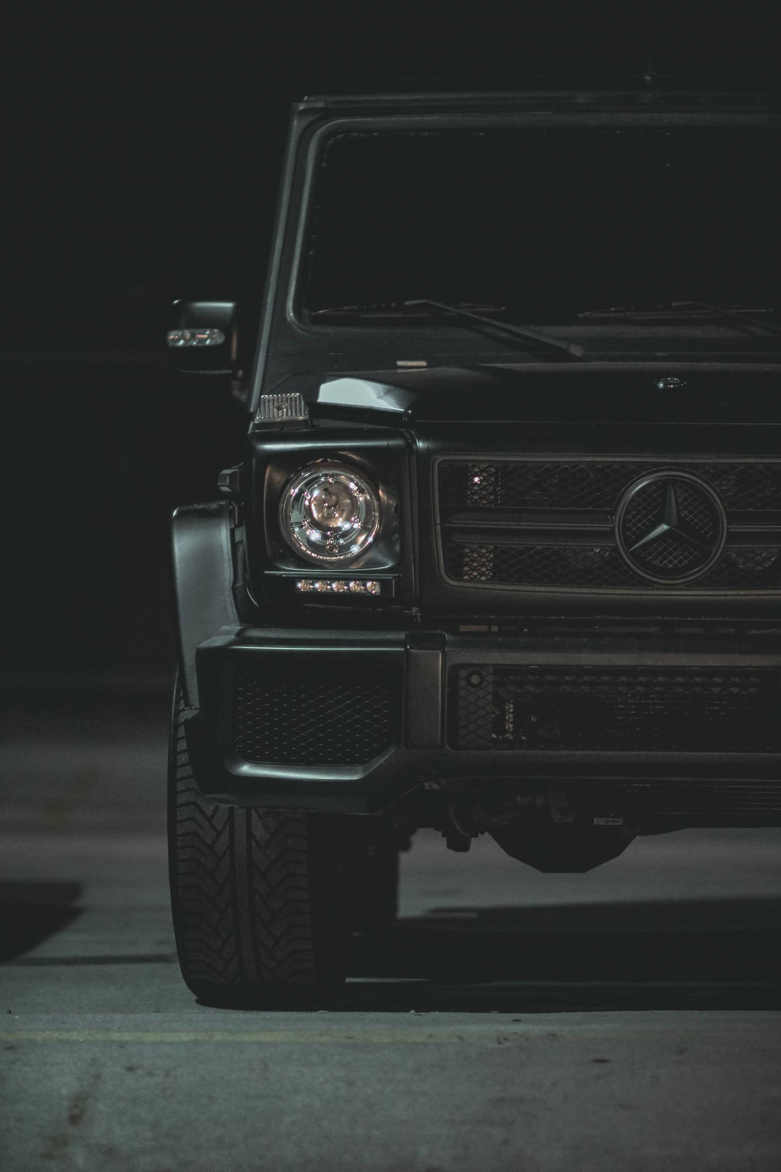 Luxury 桌布 壁紙 — 一部時尚的黑色 Mercedes G-Wagen 在夜間被戲劇性地照亮，其標誌性水箱護罩和圓形頭燈在黑暗的城市背景下發光。