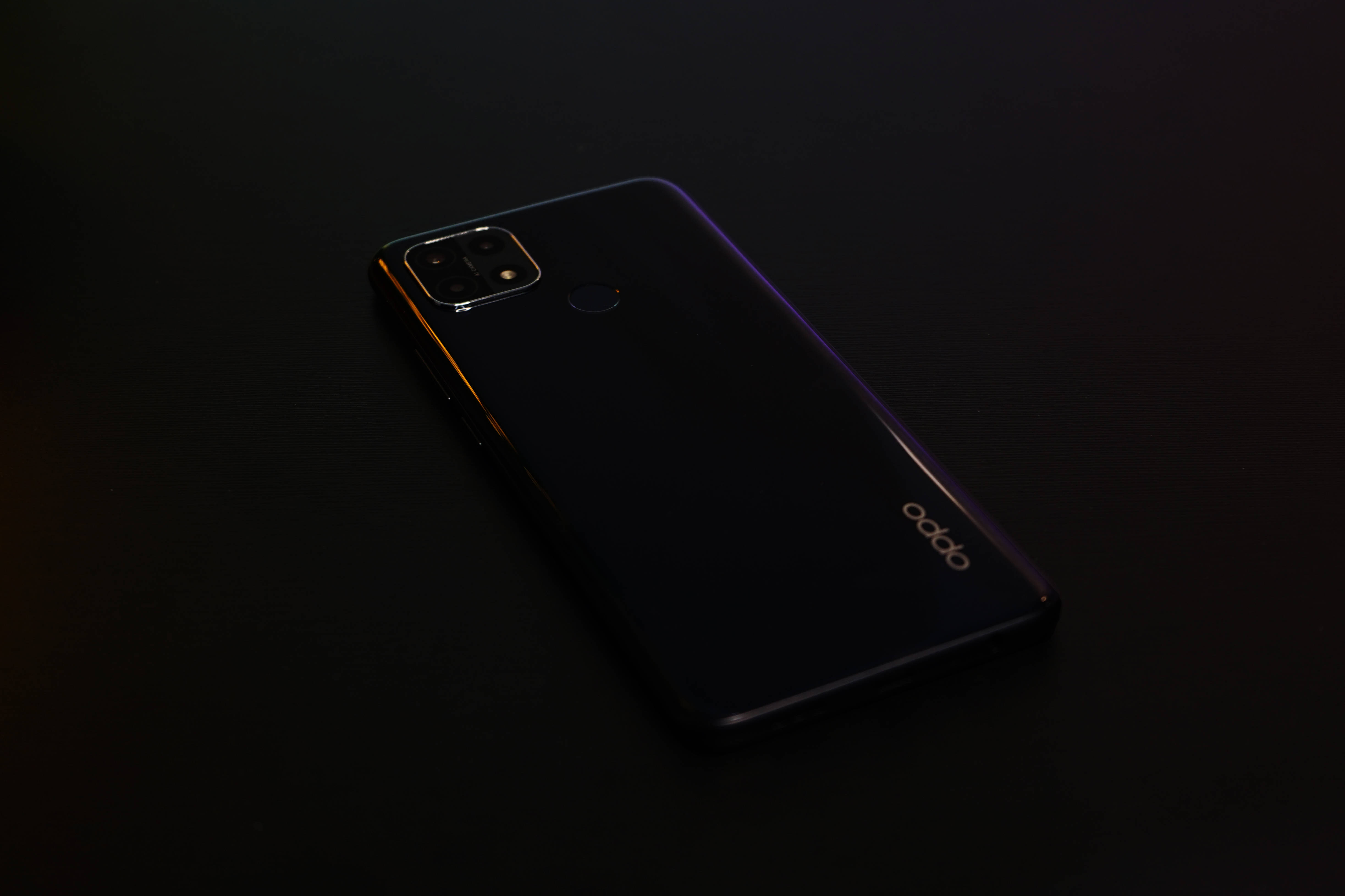 oppo 桌布 壁紙 — 一部時尚的黑色 OPPO 智慧型手機對角放置在黑暗的表面上，由微妙的環境光照明，突出其光面機身和相機模組。