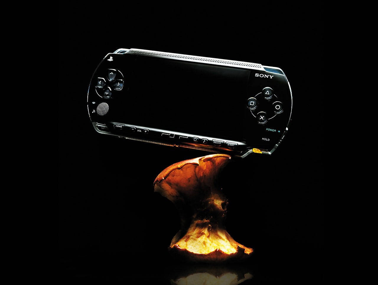 PlayStation 桌布 壁紙 — 一部時尚的黑色 Sony PSP 主機平衡在發光的橙色蘑菇上，背景為漆黑一片。