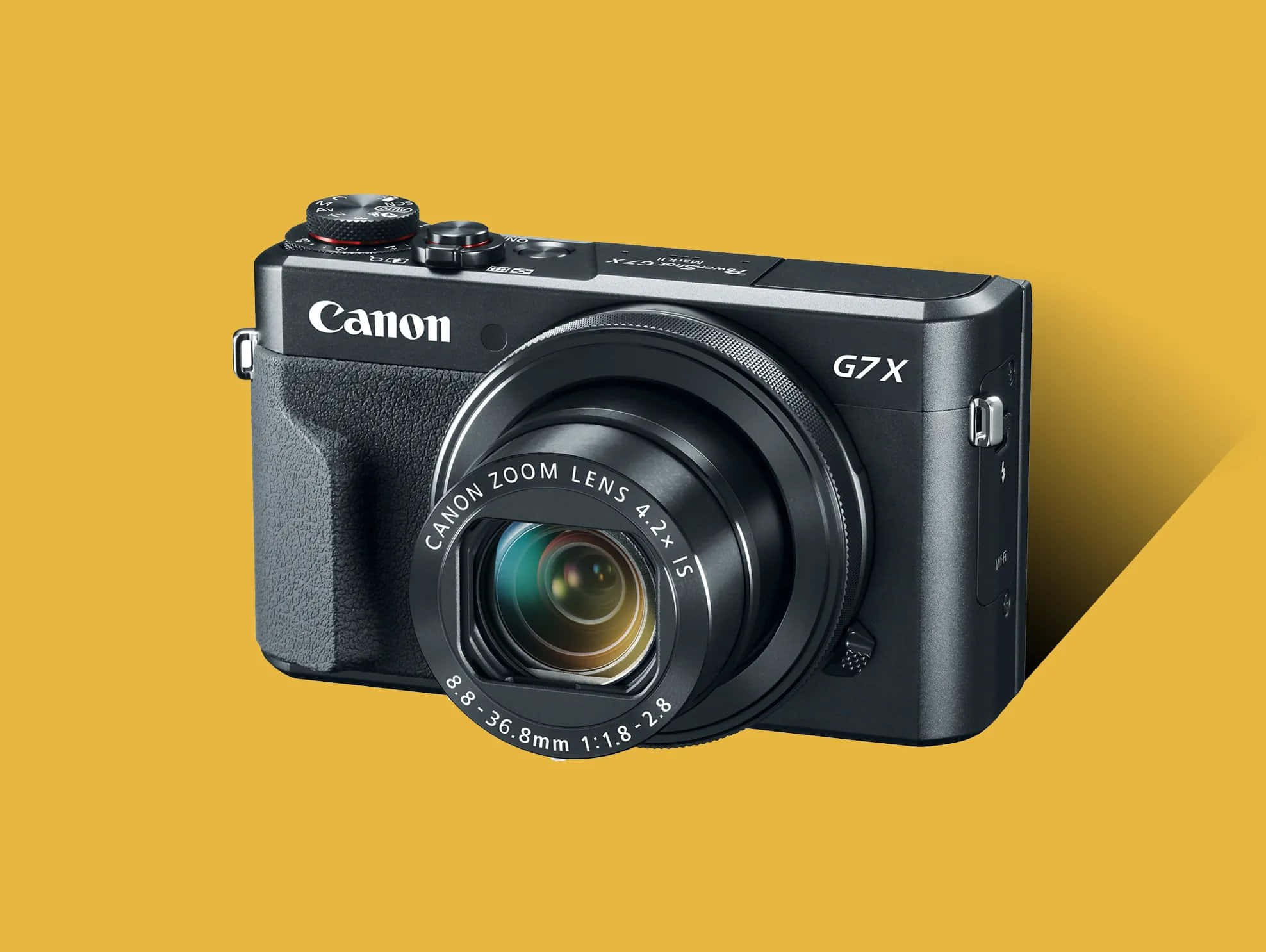 相機 桌布 壁紙 — 一部時尚的黑色Canon G7X輕便相機配備變焦鏡頭，傾斜放置在純芥末黃色背景上。