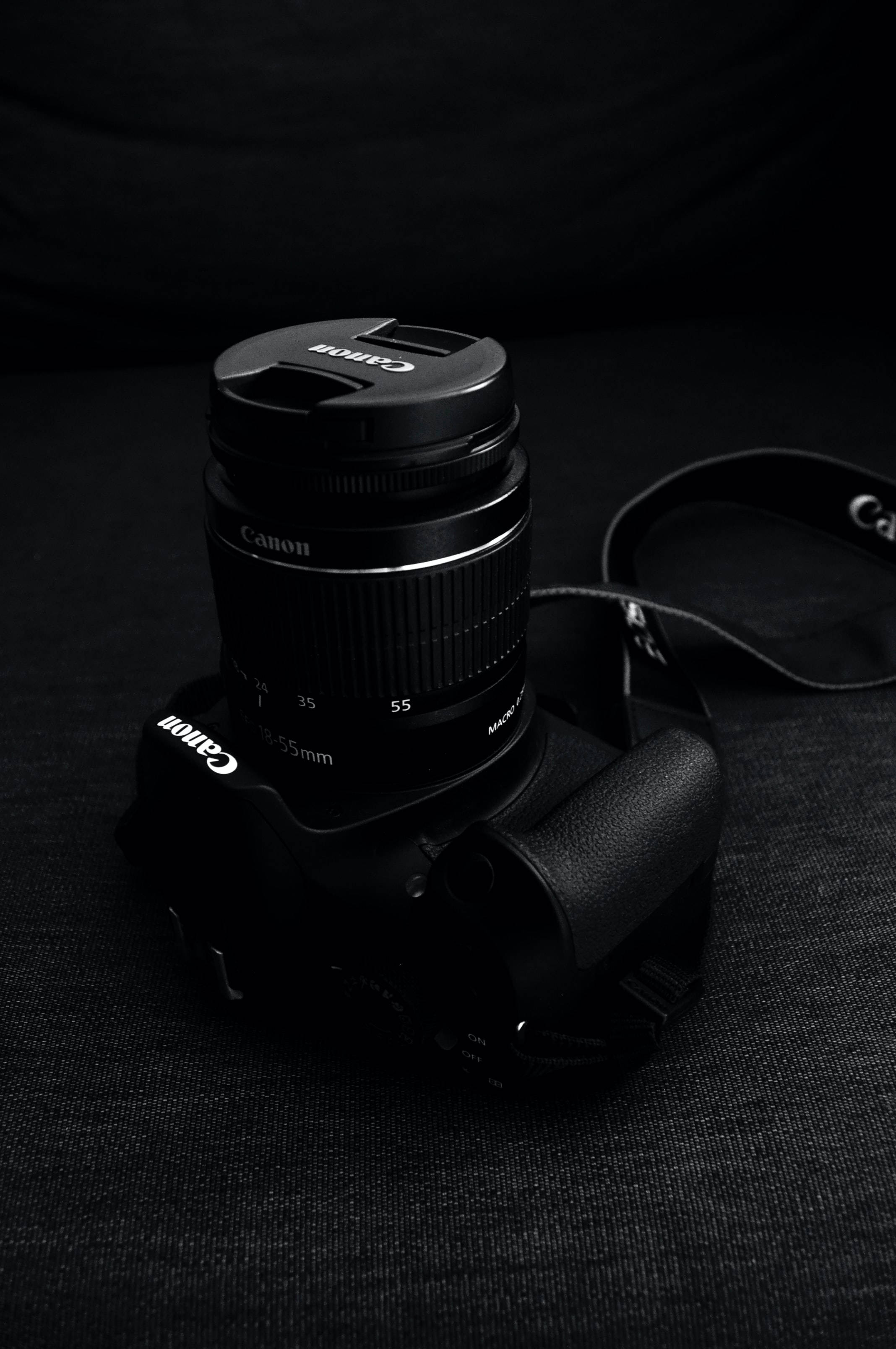 科技動圖 桌布 壁紙 — 一部時尚的黑色Canon相機，配備35-55mm鏡頭，在戲劇性的低調燈光下放置在深色布料上。