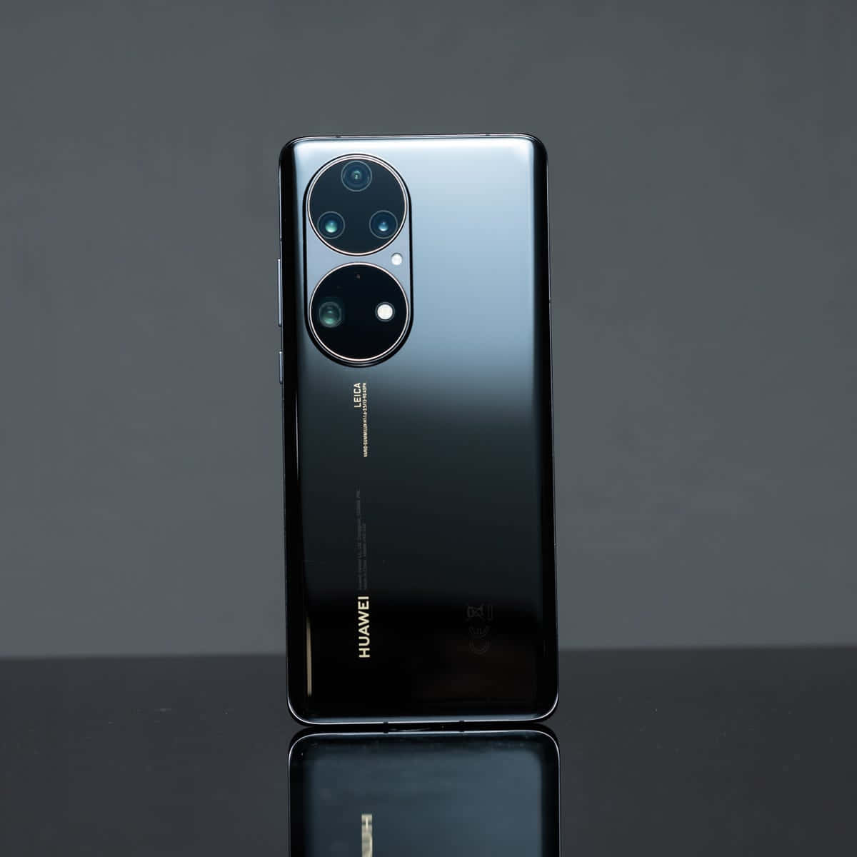 華為 桌布 壁紙 — 一部時尚的黑色Huawei智慧型手機，帶有圓形相機模組，直立於反光表面上，背景為柔和的灰色。
