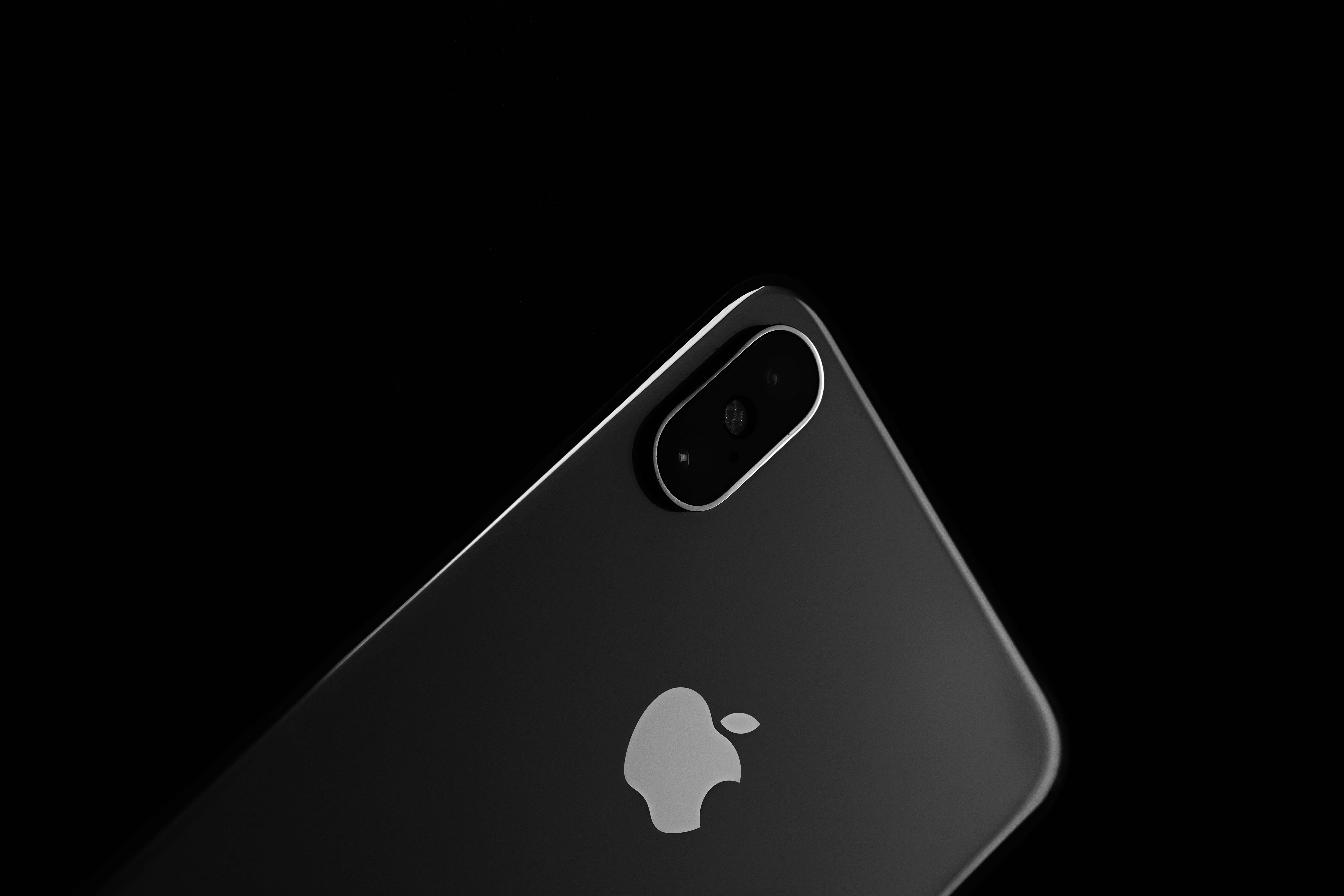 iPhone XS 桌布 壁紙 — 一部時尚的黑色iPhone，帶有銀色Apple標誌和雙攝像頭模組，傾斜在純黑色背景上。