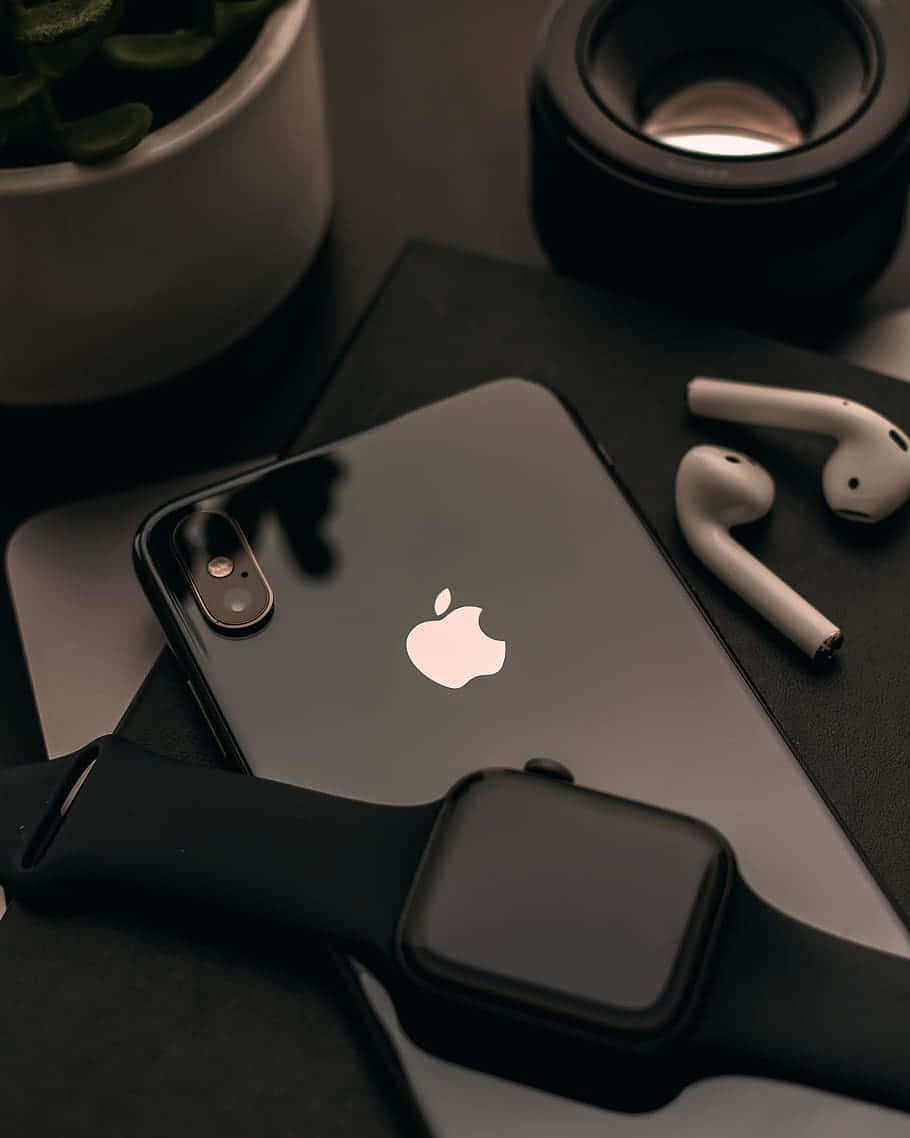 蘋果 桌布 壁紙 — 一部時尚的黑色iPhone和Apple Watch與白色AirPods和盆栽植物一起放在深色桌子上。