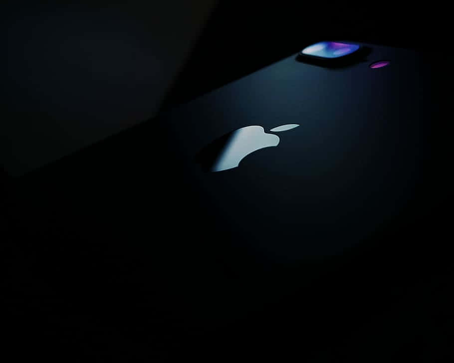 桌布 壁紙 — 一部時尚的黑色iPhone在黑暗中背光，帶有發光的Apple標誌和相機模組。
