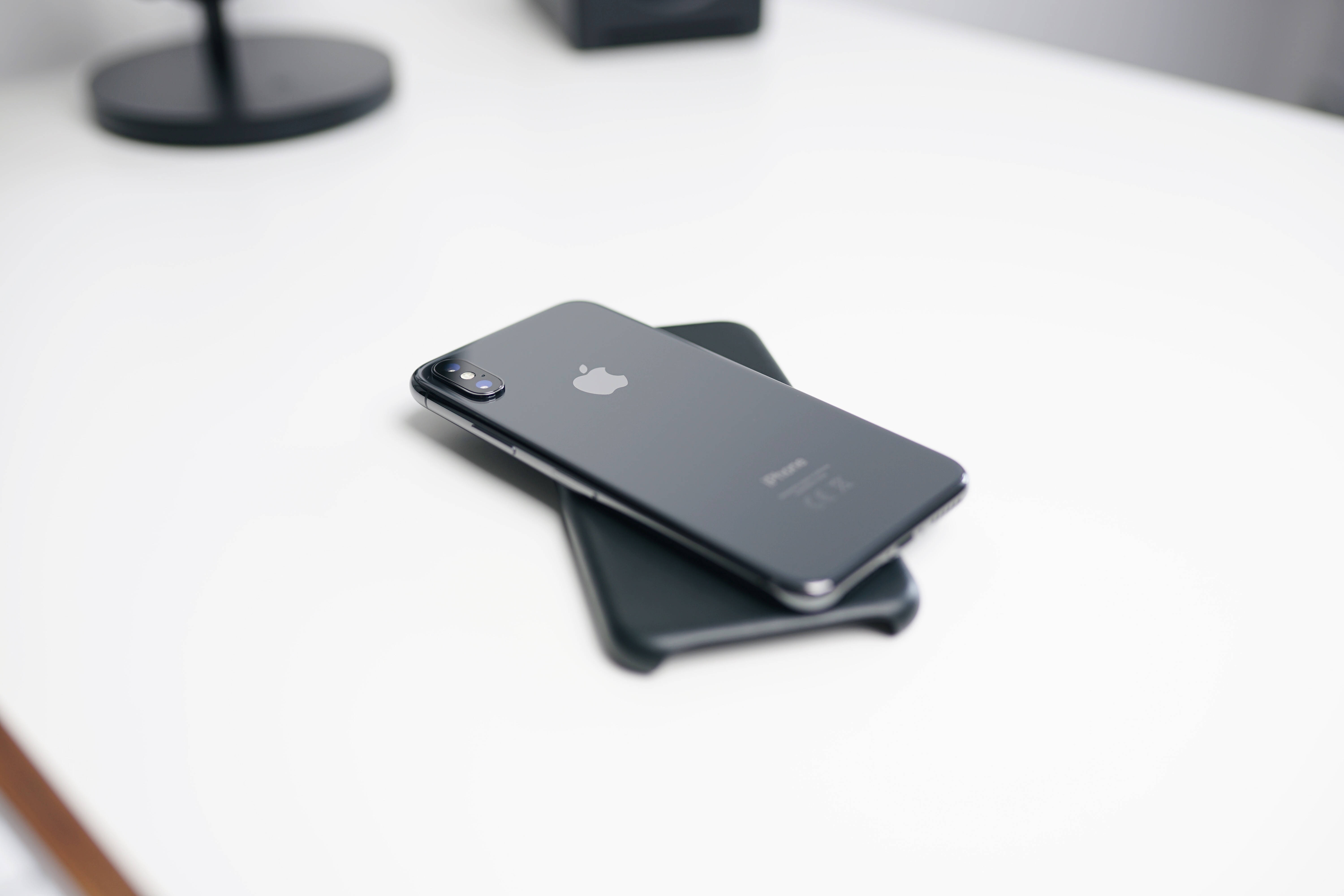 iOS 桌布 壁紙 — 一部時尚的黑色iPhone放在另一部手機上，置於簡約白色桌面，帶有柔和陰影。