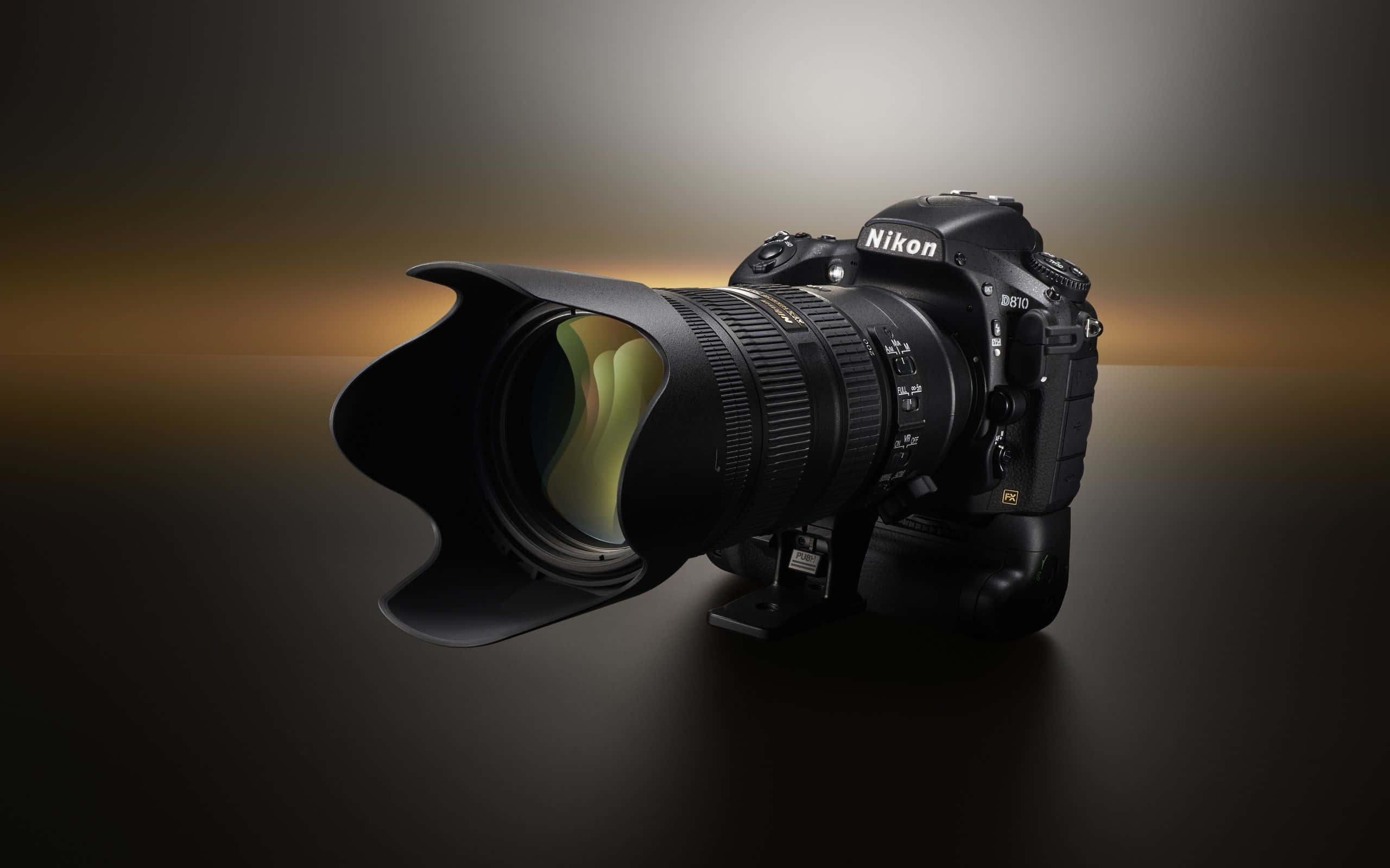 攝影 桌布 壁紙 — 一部時尚的黑色Nikon D810 DSLR相機，配備大型望遠鏡頭和花瓣形遮光罩，在溫暖的漸變燈光下放置在深色反光表面上。