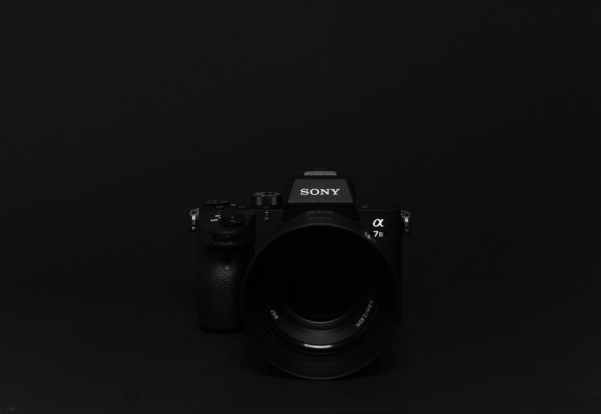 黑色 桌布 壁紙 — 一部時尚的黑色Sony Alpha 7 III相機，在極簡純黑背景下以柔和工作室燈光居中展示。