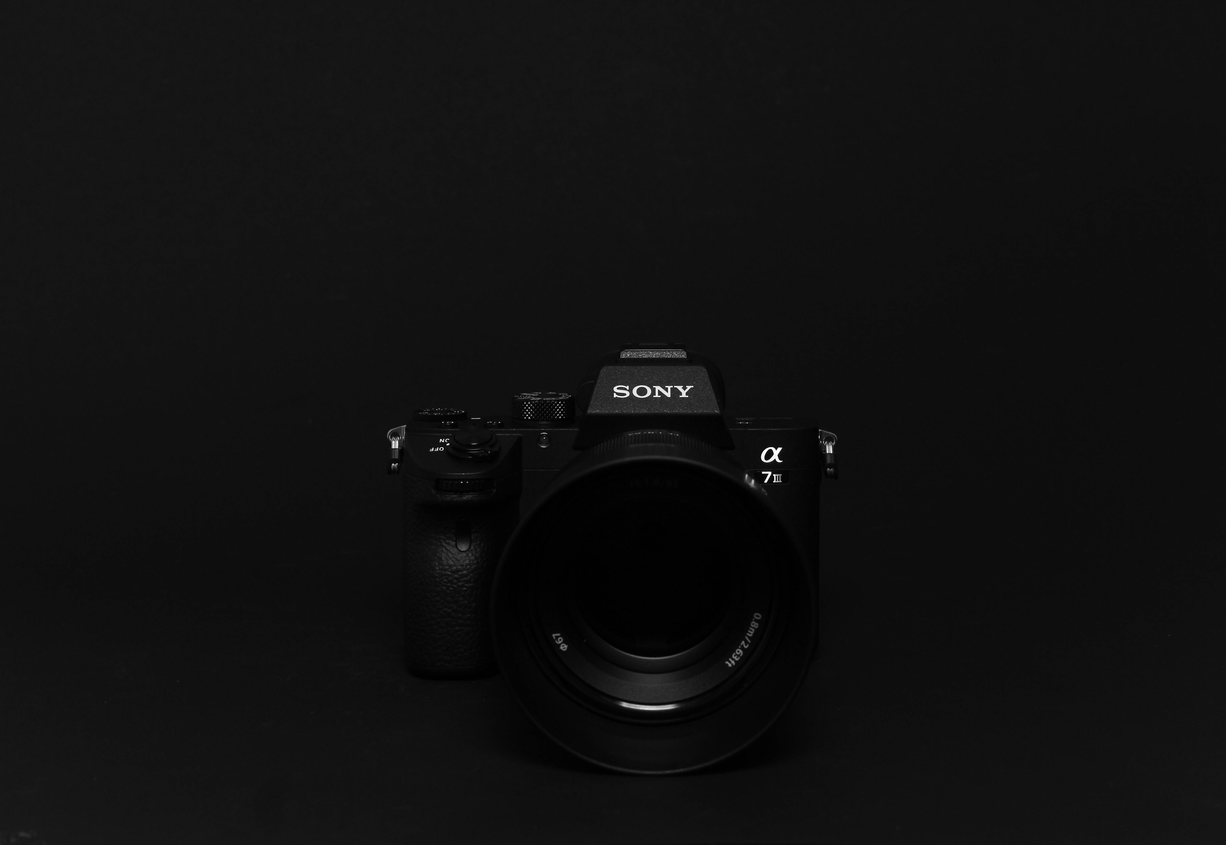 Screen 桌布 壁紙 — 一部時尚的黑色Sony Alpha 7 III相機，在極簡純黑背景上居中，帶有柔和的工作室燈光。