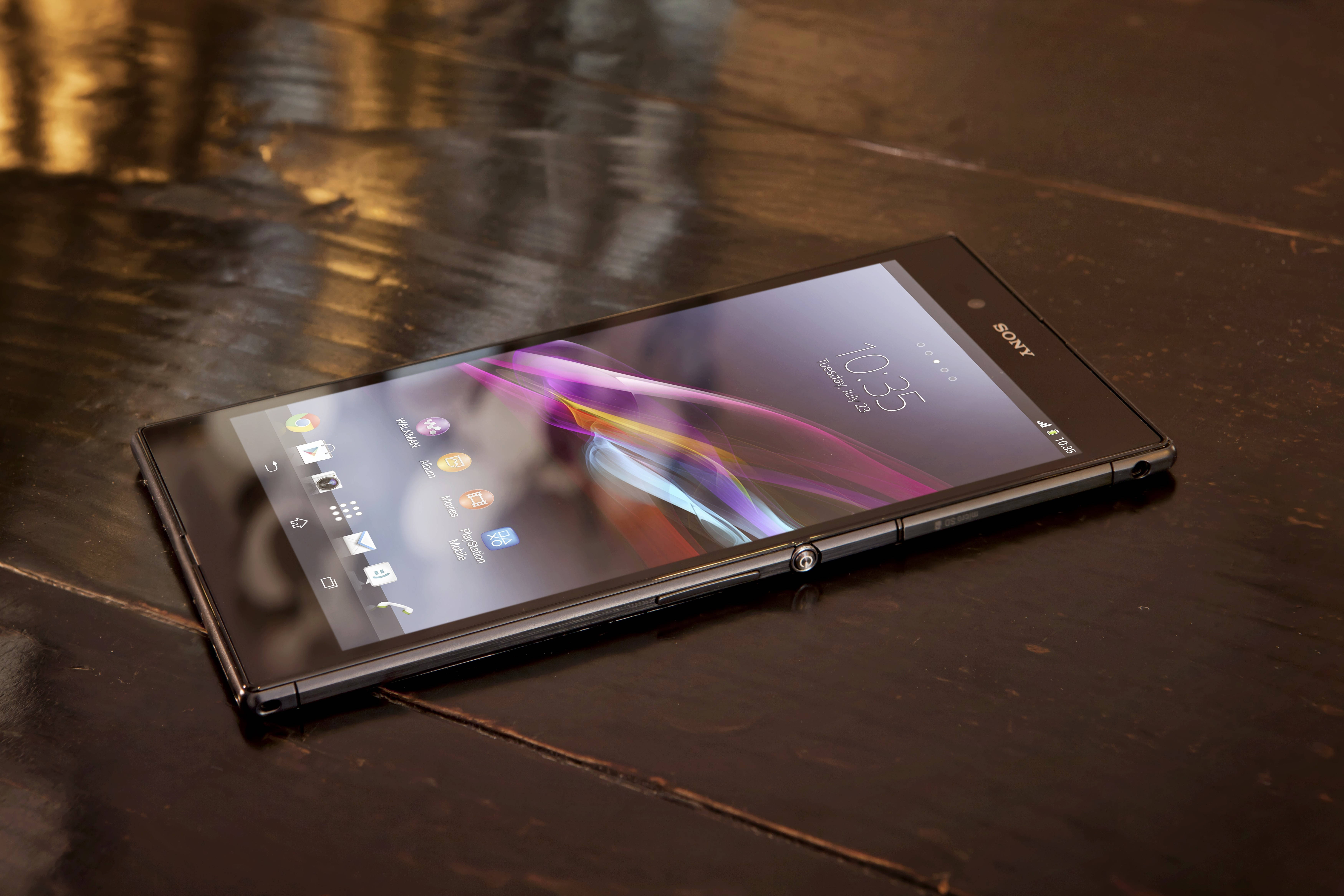 Sony 桌布 壁紙 — 一部時尚的黑色Sony智慧型手機，帶有彩色抽象桌布，對角放置在深色木質表面上。