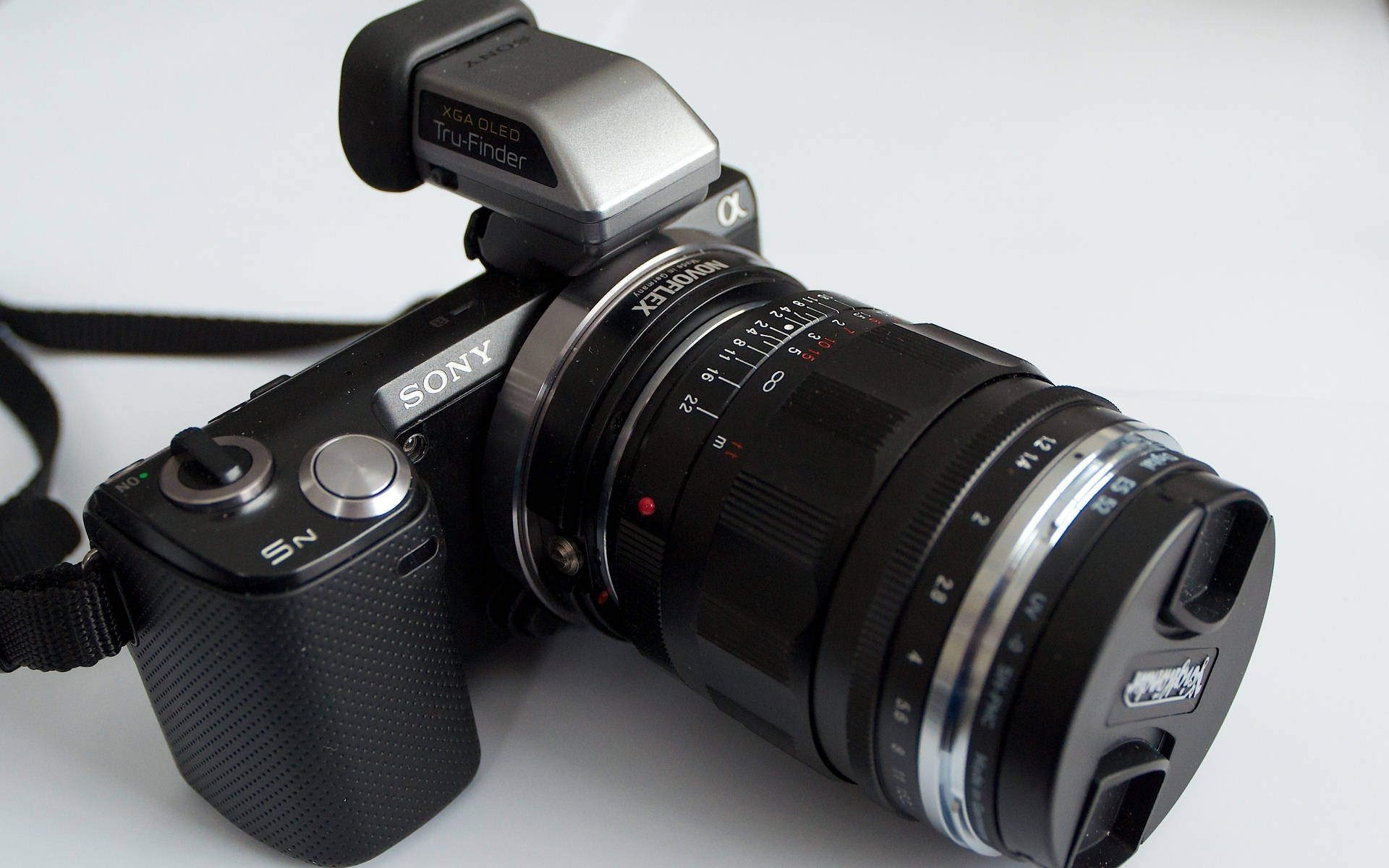 Sony 桌布 壁紙 — 一部時尚的黑色Sony無反相機，配有安裝的鏡頭和XGA OLED Tru-Finder，傾斜放置在純白色表面上。