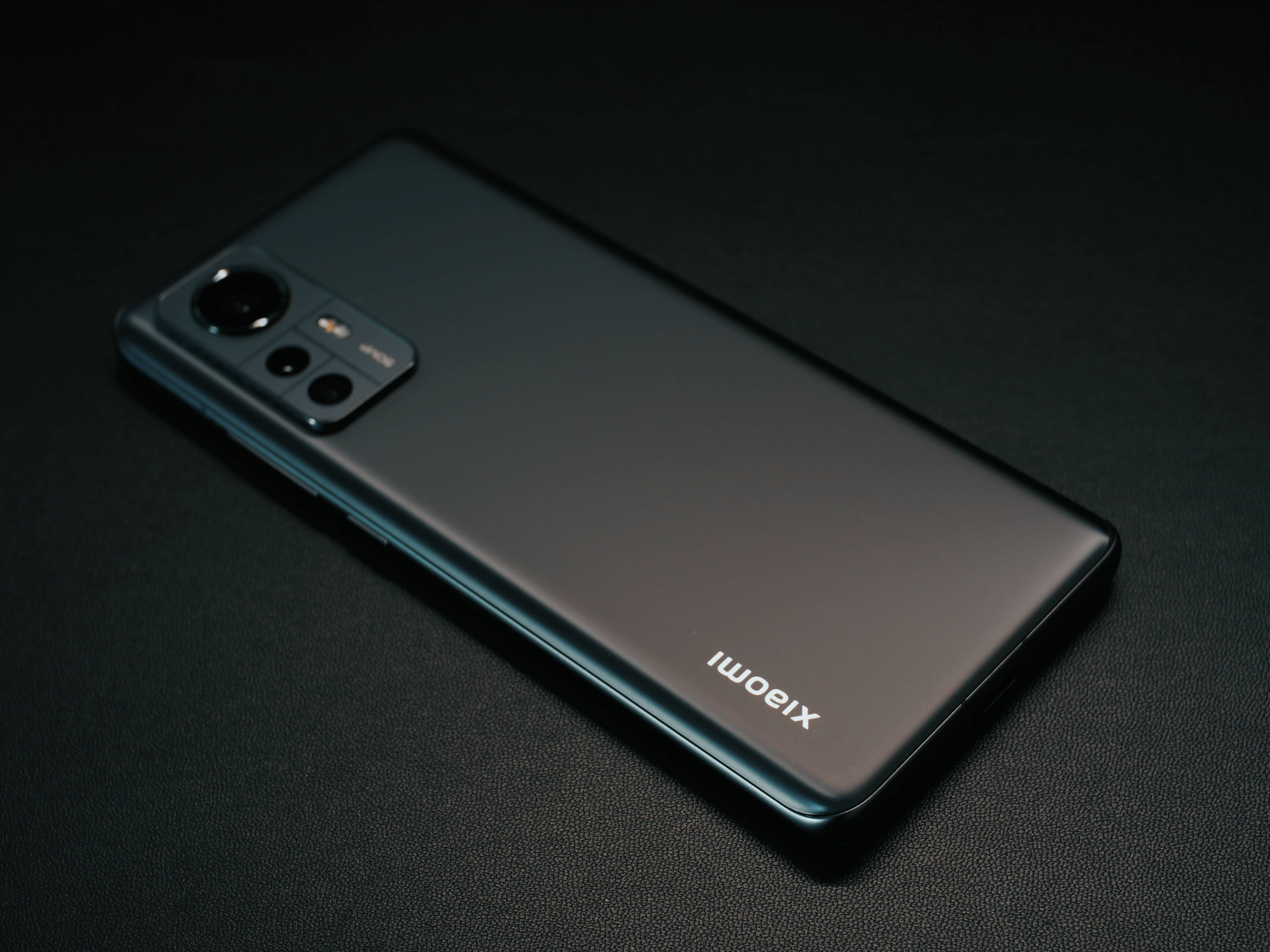Xiaomi 桌布 壁紙 — 一部時尚的黑色Xiaomi智慧型手機在戲劇性的工作室燈光下對角放置在深色紋理表面上。