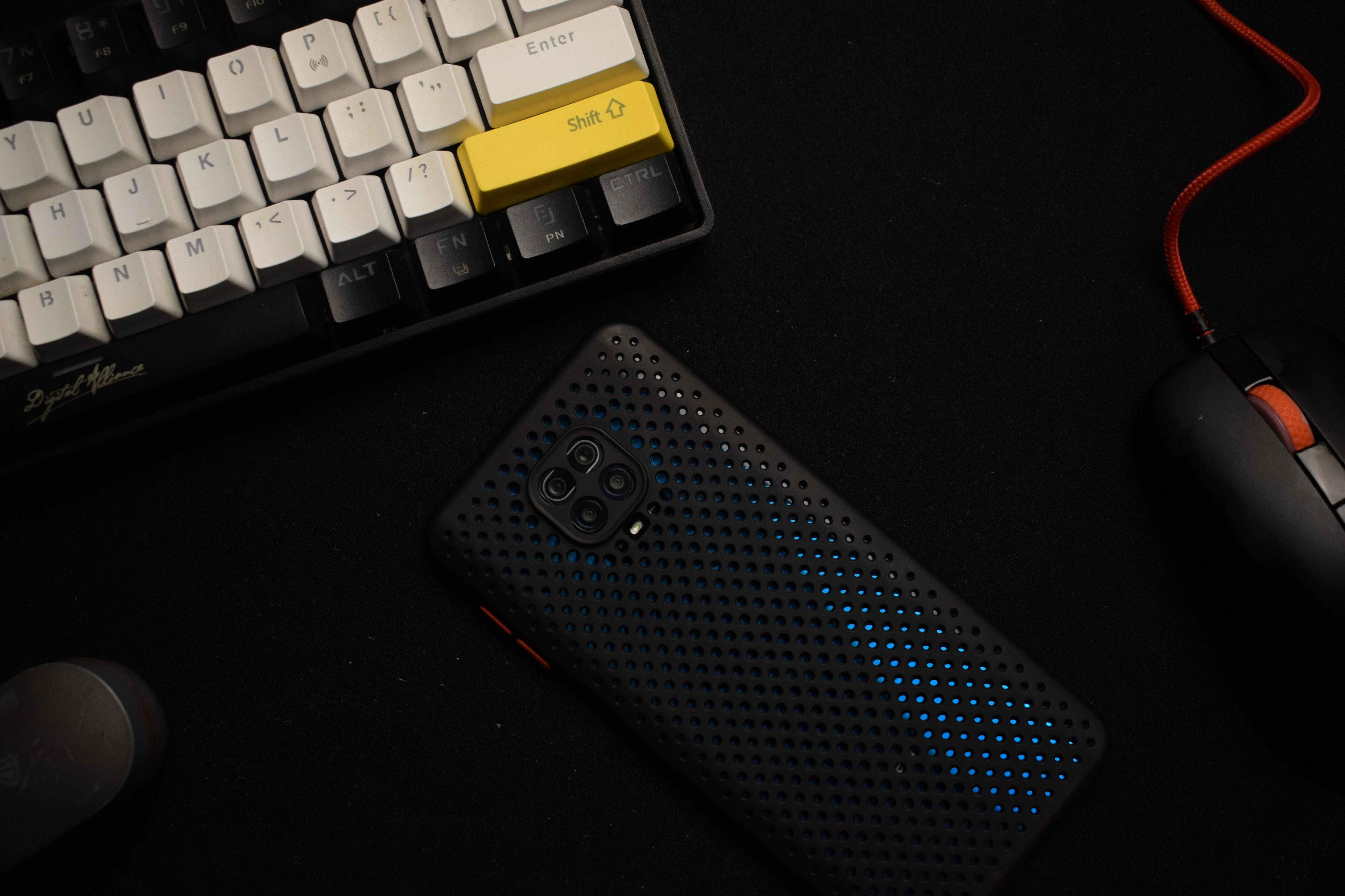 Xiaomi 桌布 壁紙 — 一部時尚的黑色手機帶有發光的藍色穿孔，旁邊放著白色鍵盤和遊戲滑鼠，在深色桌子上。