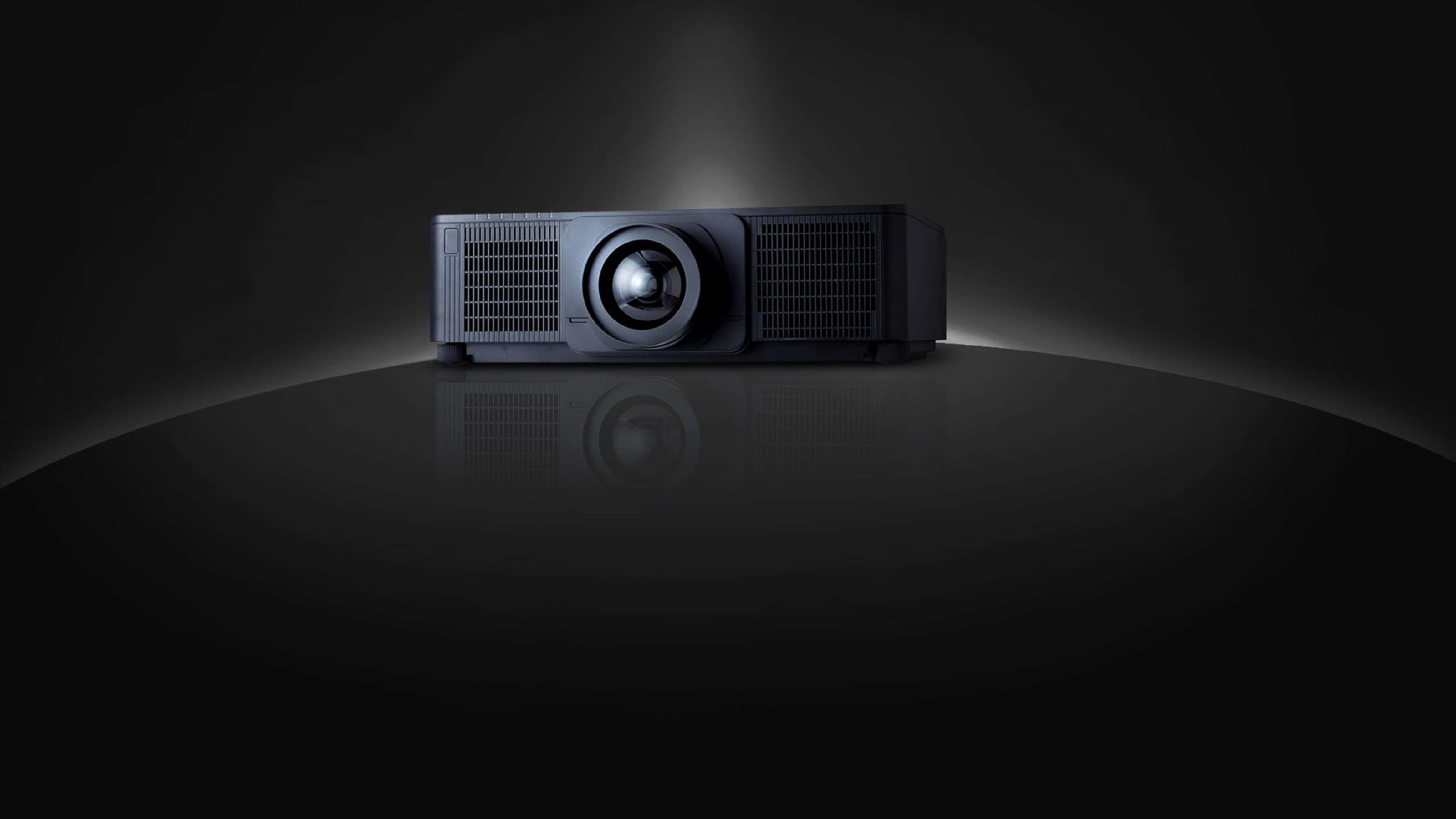 4K Projector 桌布 壁紙 — 一部時尚的黑色投影機置於反光表面中央，在黑暗背景下投射出柔和的光芒。