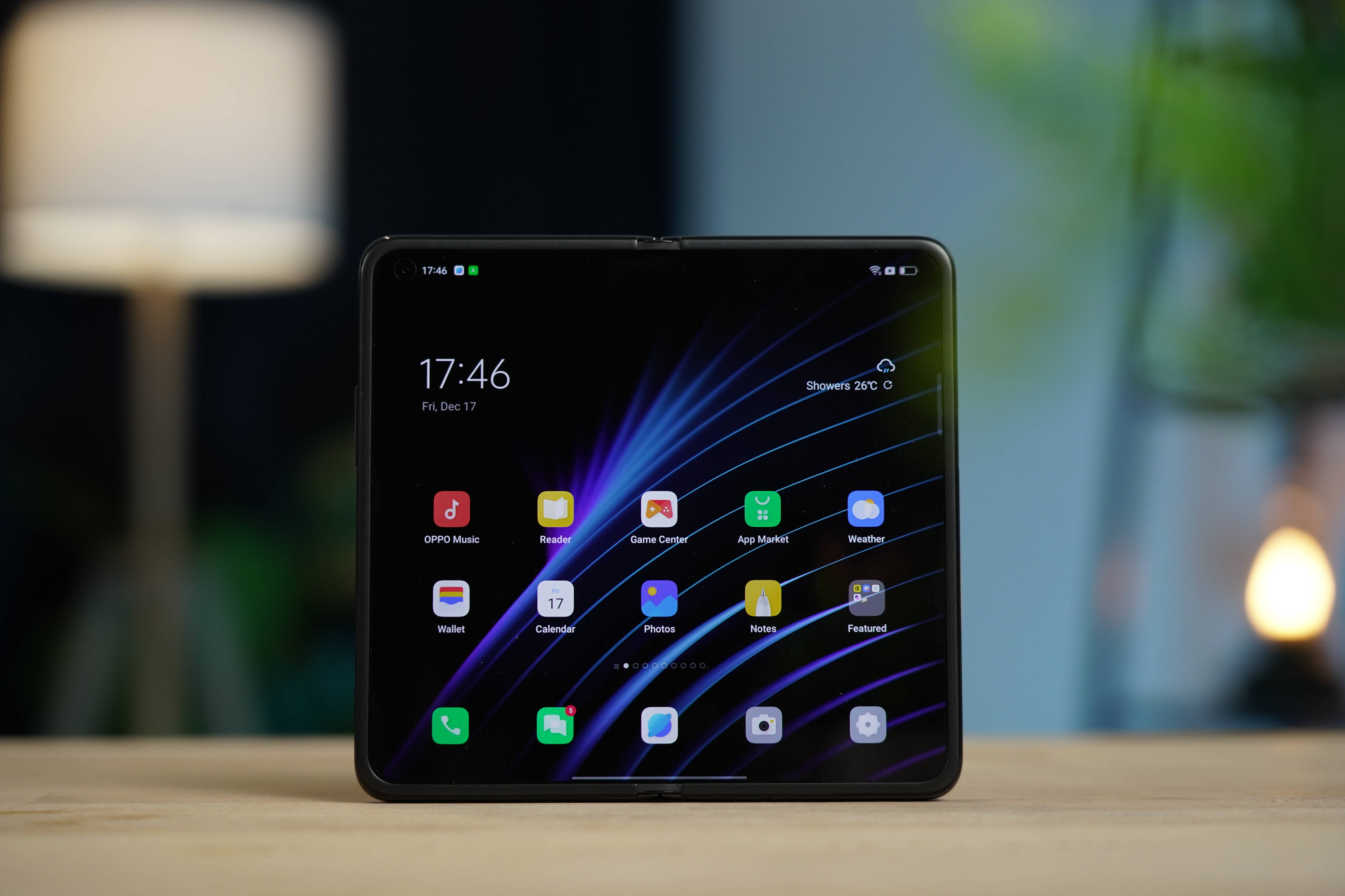 oppo 桌布 壁紙 — 一部時尚的黑色摺疊智慧型手機在木桌上顯示充滿活力的應用程式網格，背景是動態的紫藍色光條壁紙，帶有柔和模糊的背景燈光。