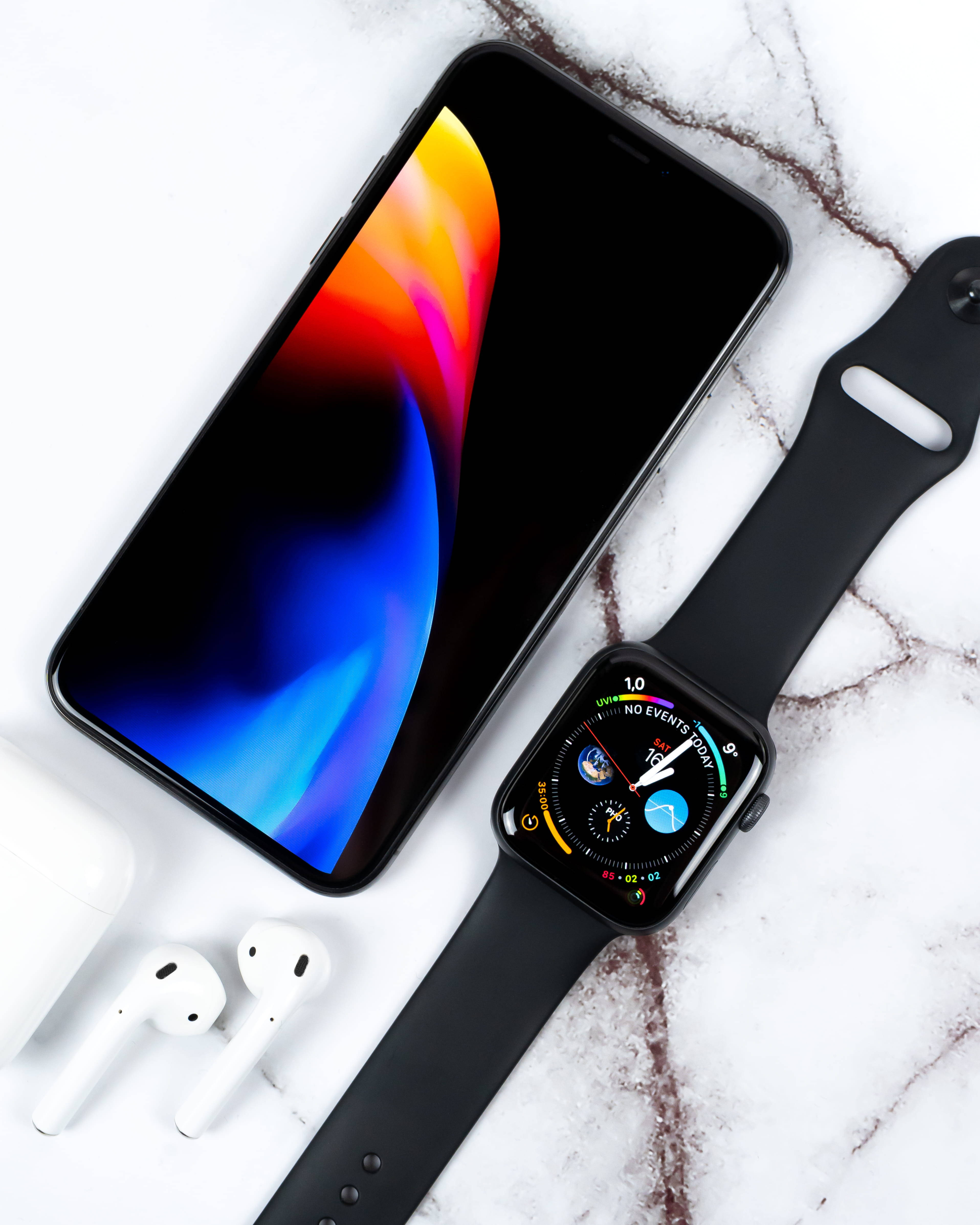 4K iPhone 11 桌布 壁紙 — 一部時尚的黑色智慧型手機和智慧手錶，搭配白色耳機，放在白色大理石表面上，展示充滿活力的抽象桌布。