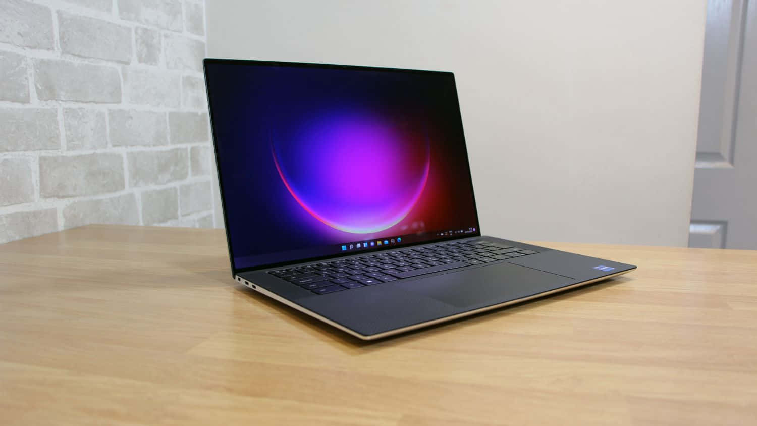 Dell 桌布 壁紙 — 一部時尚的黑色筆記型電腦，帶有充滿活力的紫色和粉紅色漸變螢幕，打開放在淺色木桌上，背景是白色磚牆。