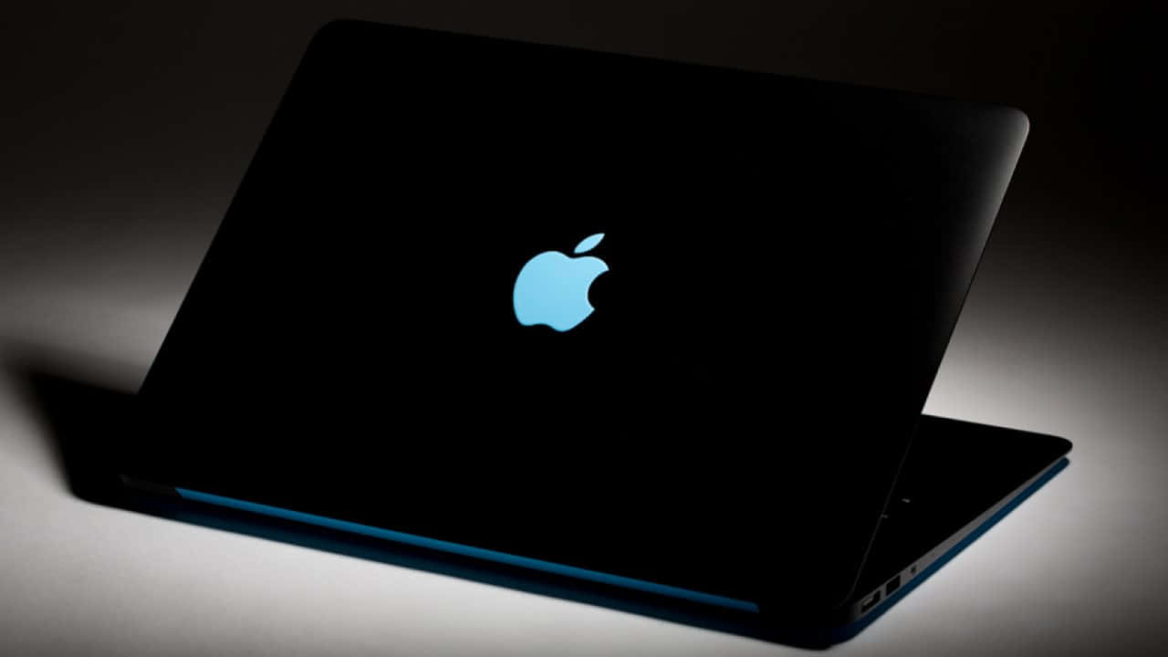 Black Macbook 桌布 壁紙 — 一部時尚的黑色筆記型電腦，帶有發光的藍色Apple標誌，在戲劇性的工作室燈光下打開。